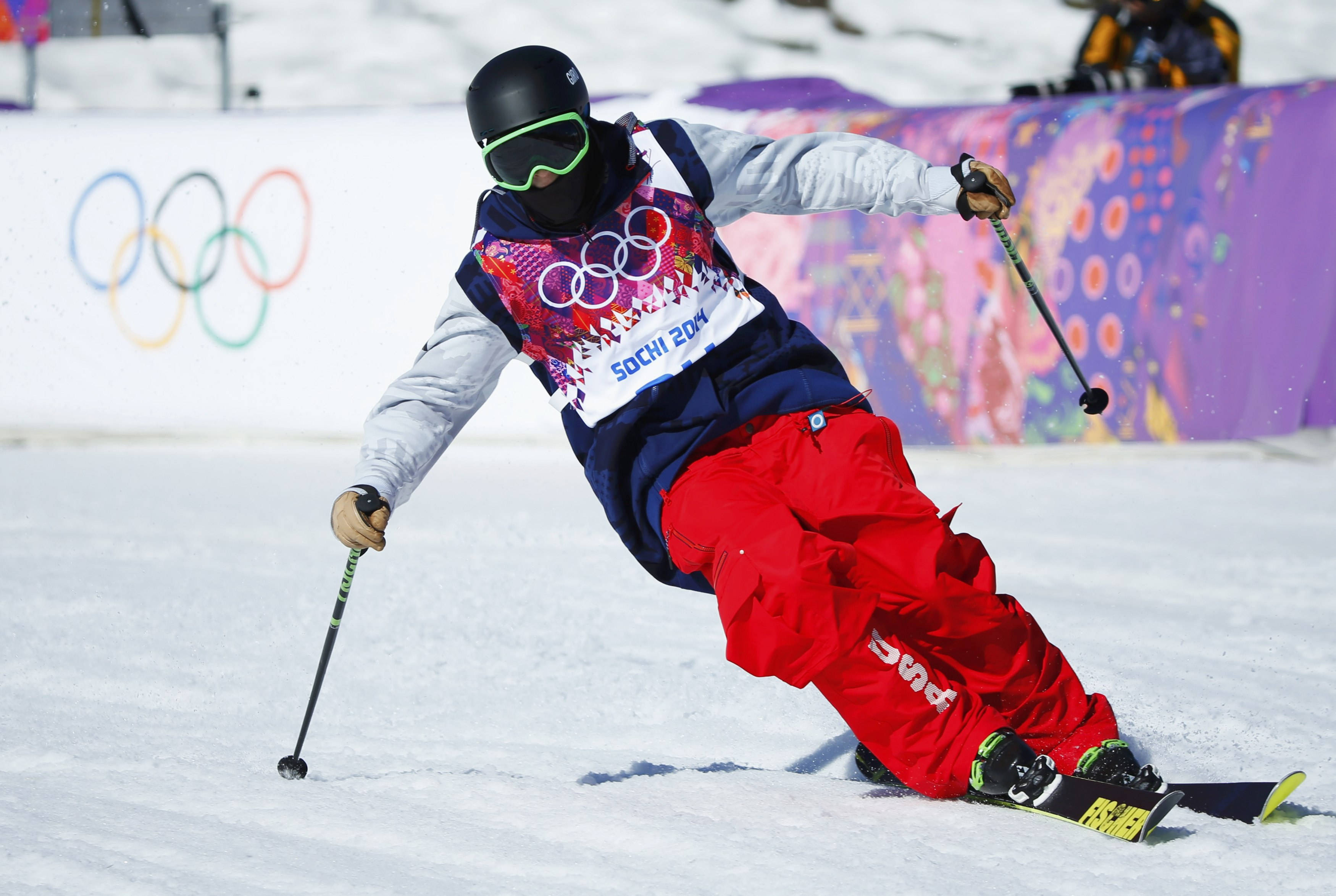 Winter Olympics 桌布 壁紙 — 一名穿著紅色褲子和黑色頭盔的滑雪運動員在索契2014年奧運會上滑雪，背景可見奧運五環。
