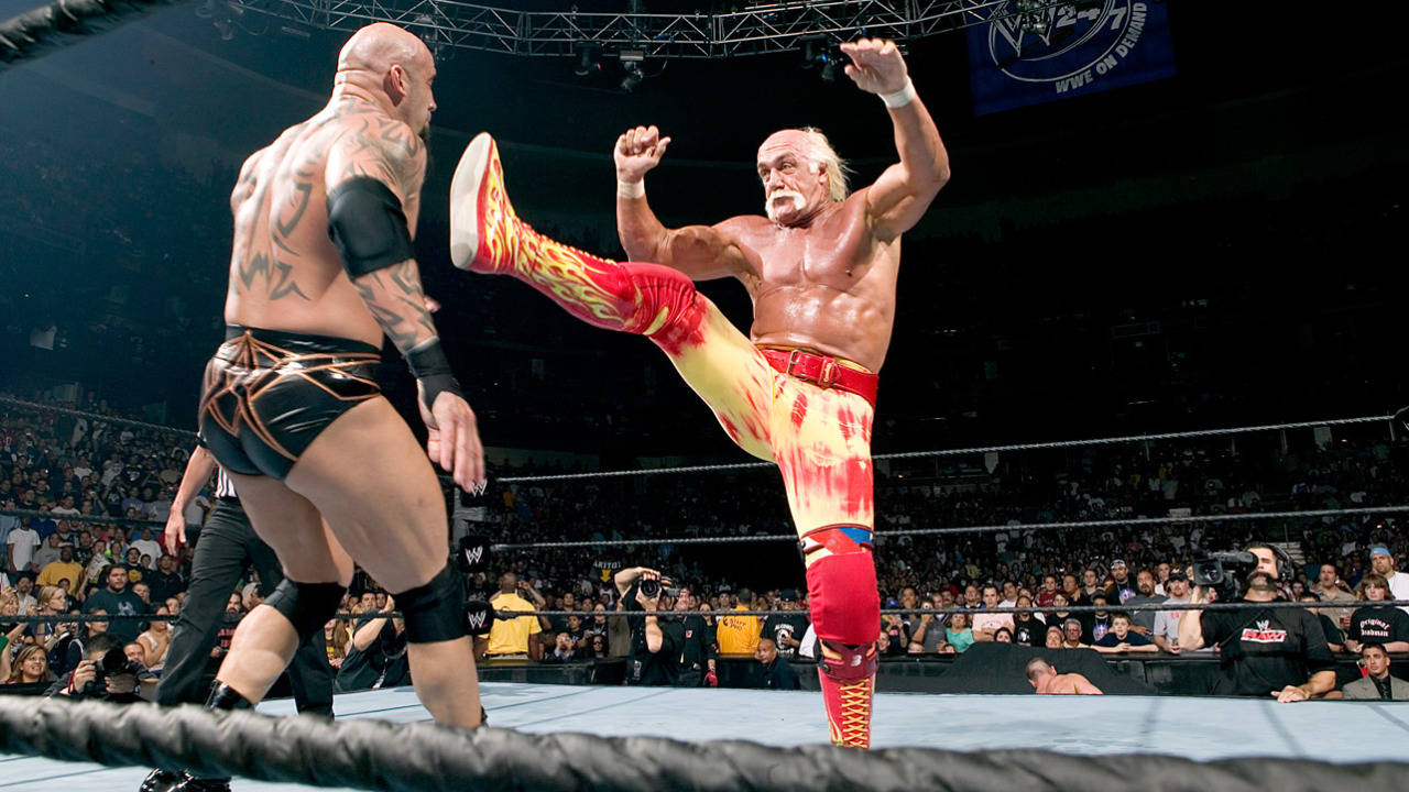 Hulk Hogan 桌布 壁紙 — 一名穿著紅黃火焰圖案緊身褲的摔角手，在燈光明亮的擂台上，對著咆哮的群眾向對手踢出一記高踢。
