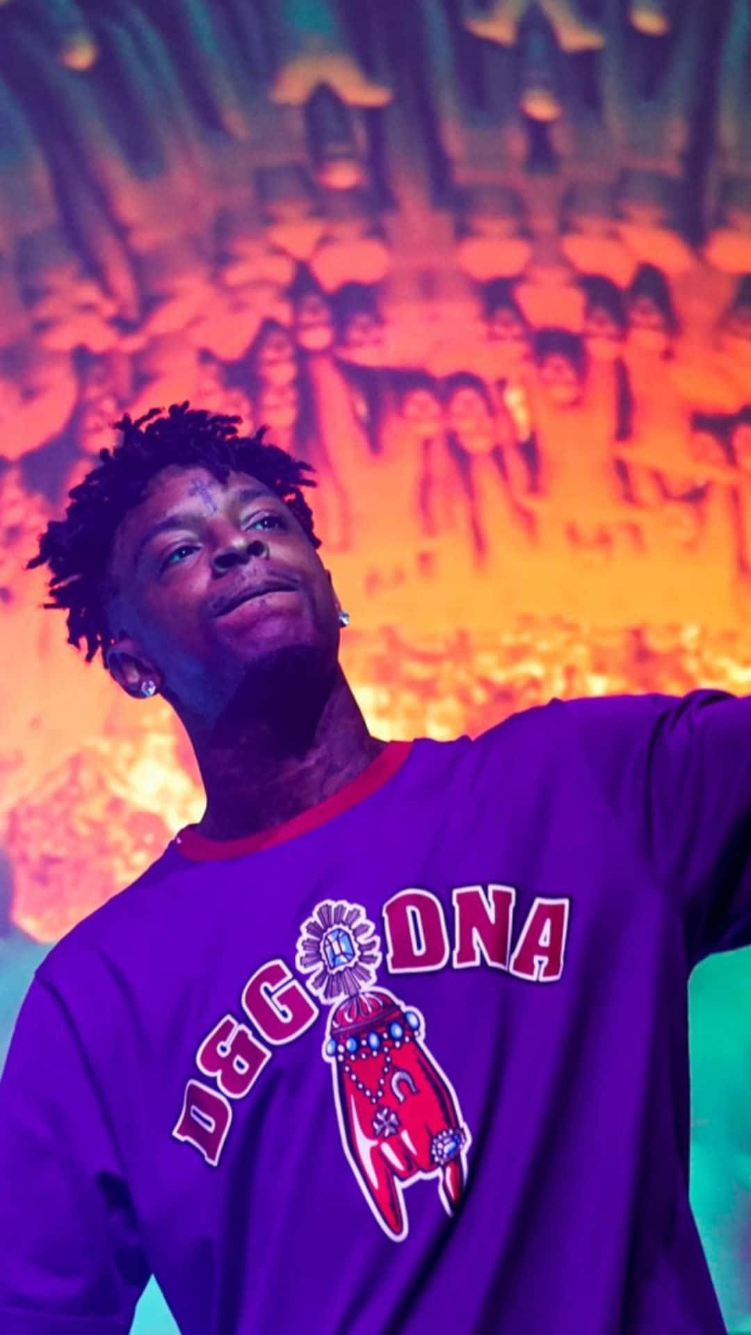 21 Savage 桌布 壁紙 — 一名穿著紫色D&G DNA連帽衫的男子在充滿活力的橙色和藍綠色音樂會背景及模糊的人群中向上微笑。