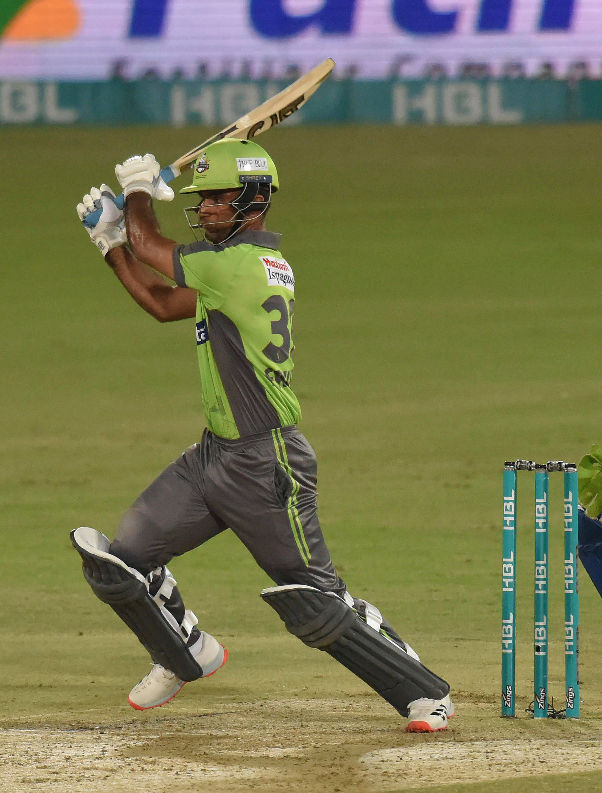 Fakhar Zaman 桌布 壁紙 — 一名穿著綠色制服的板球擊球手在體育場燈光下的夜間比賽中強力揮動球棒。