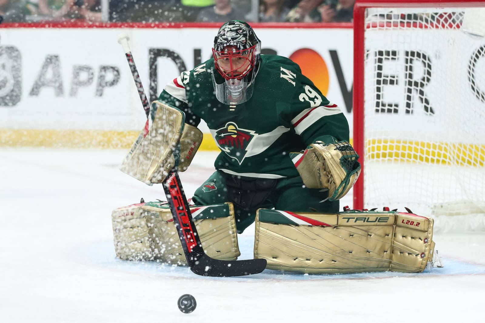 hockey 桌布 壁紙 — 一名穿著綠色裝備的冰球守門員在比賽期間，在冰上低蹲，雪花在他周圍飄落。