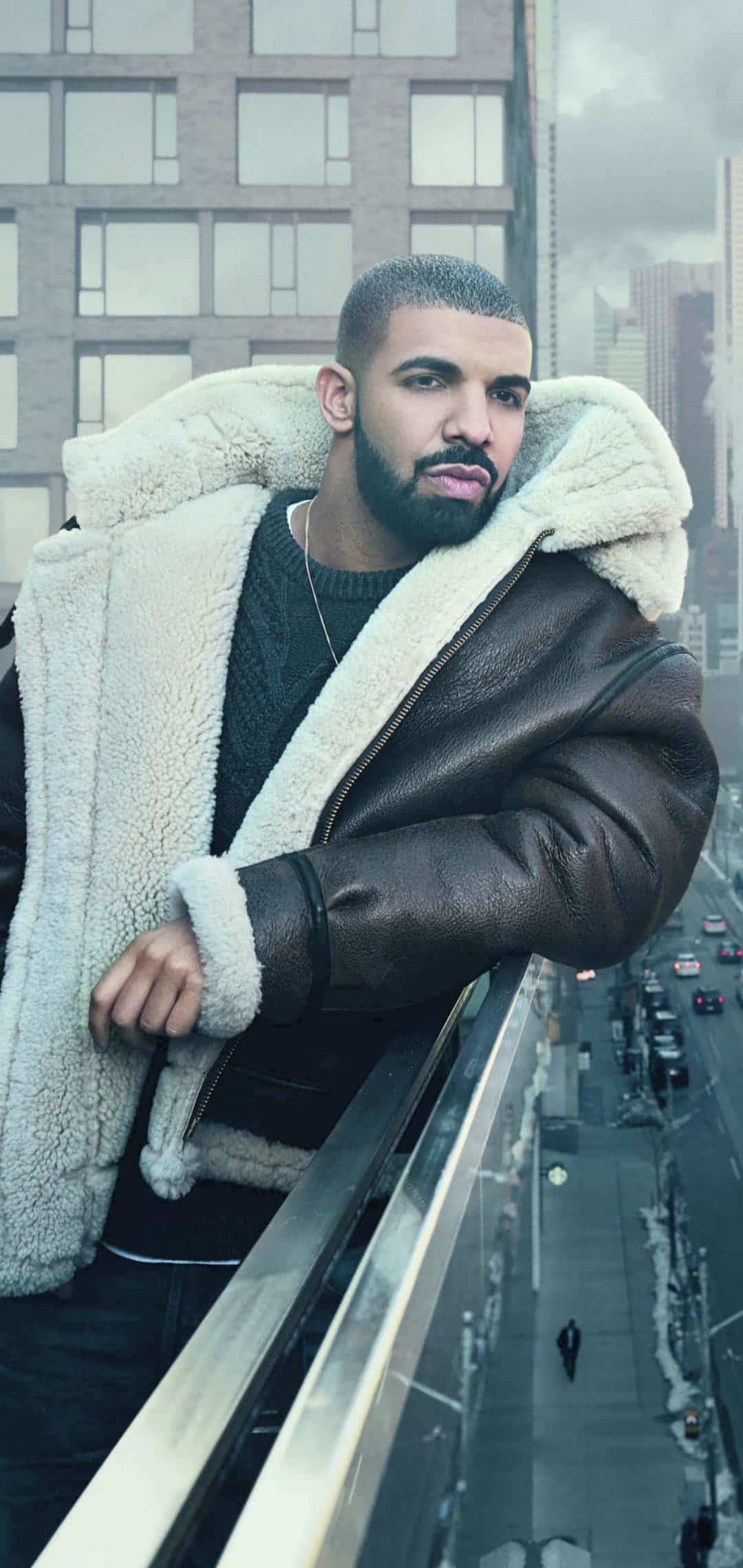 Aesthetic Drake 桌布 壁紙 — 一名穿著羊皮襯裡皮夾克的男子倚在高層大廈的陽台上，俯瞰下方繁忙的街道。