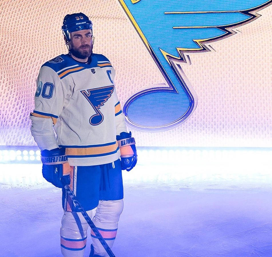 hockey 桌布 壁紙 — 一名穿著聖路易斯藍調隊球衣的冰球運動員站在冰上，球隊標誌在他身後發光。