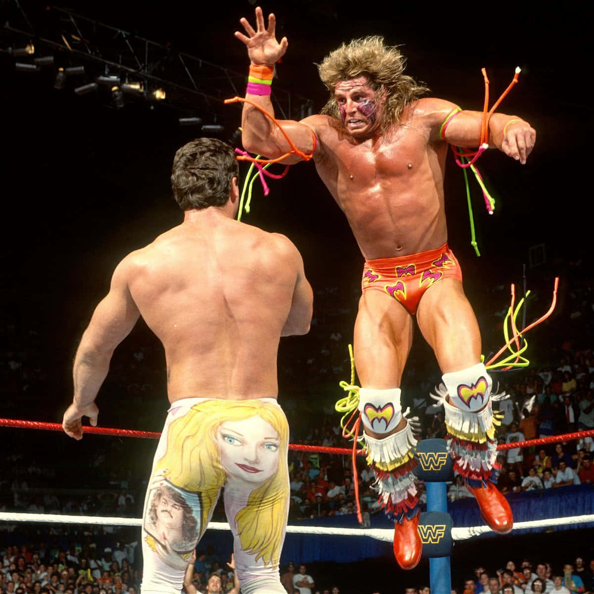 ultimate warrior 桌布 壁紙 — 一名穿著色彩繽紛服裝的摔角手從角柱跳向對手，場館內座無虛席。