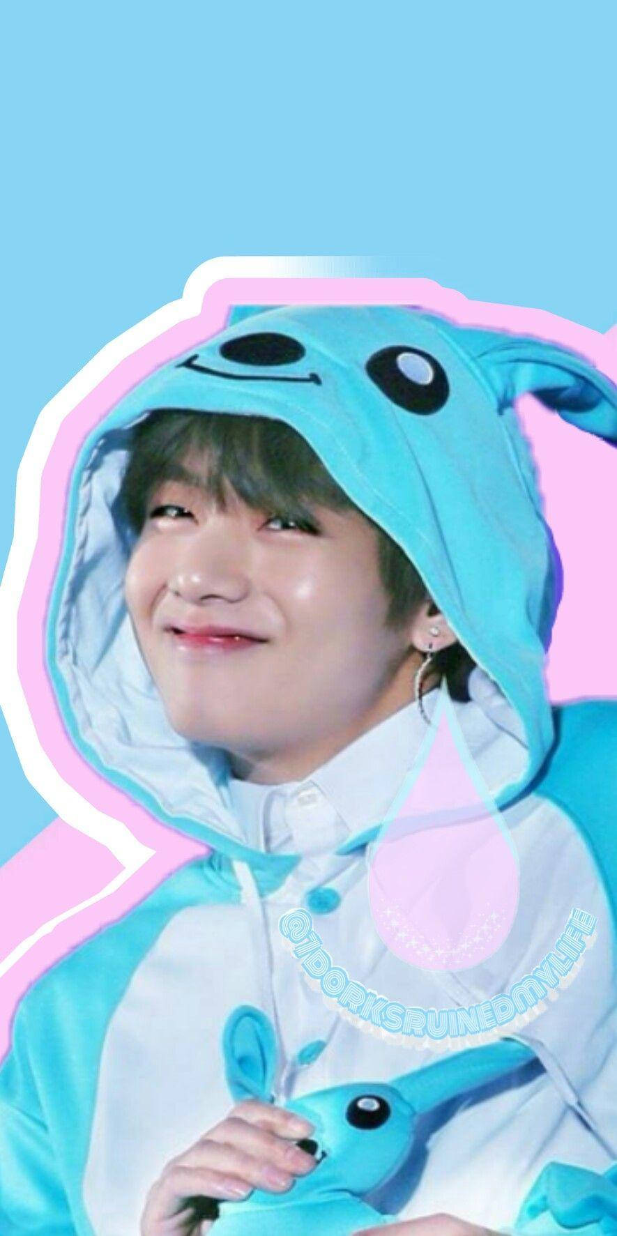 Taehyung Cute 桌布 壁紙 — 一名穿著藍色兔子連身衣的年輕男子在粉紅色和藍色粉彩背景前溫暖地微笑。