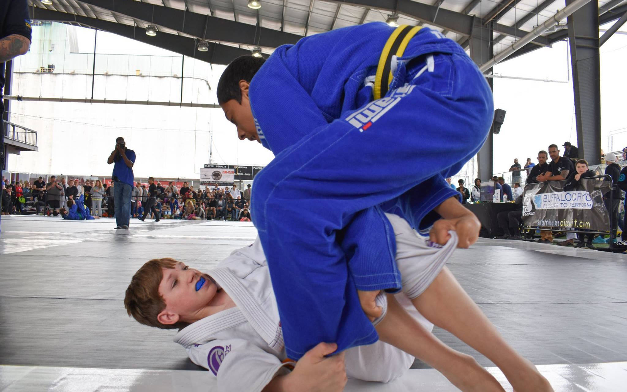 martial arts 桌布 壁紙 — 一名穿著藍色柔道服的年輕柔道選手在比賽中對一名穿著白色柔道服的對手執行一個動態的投擲動作。