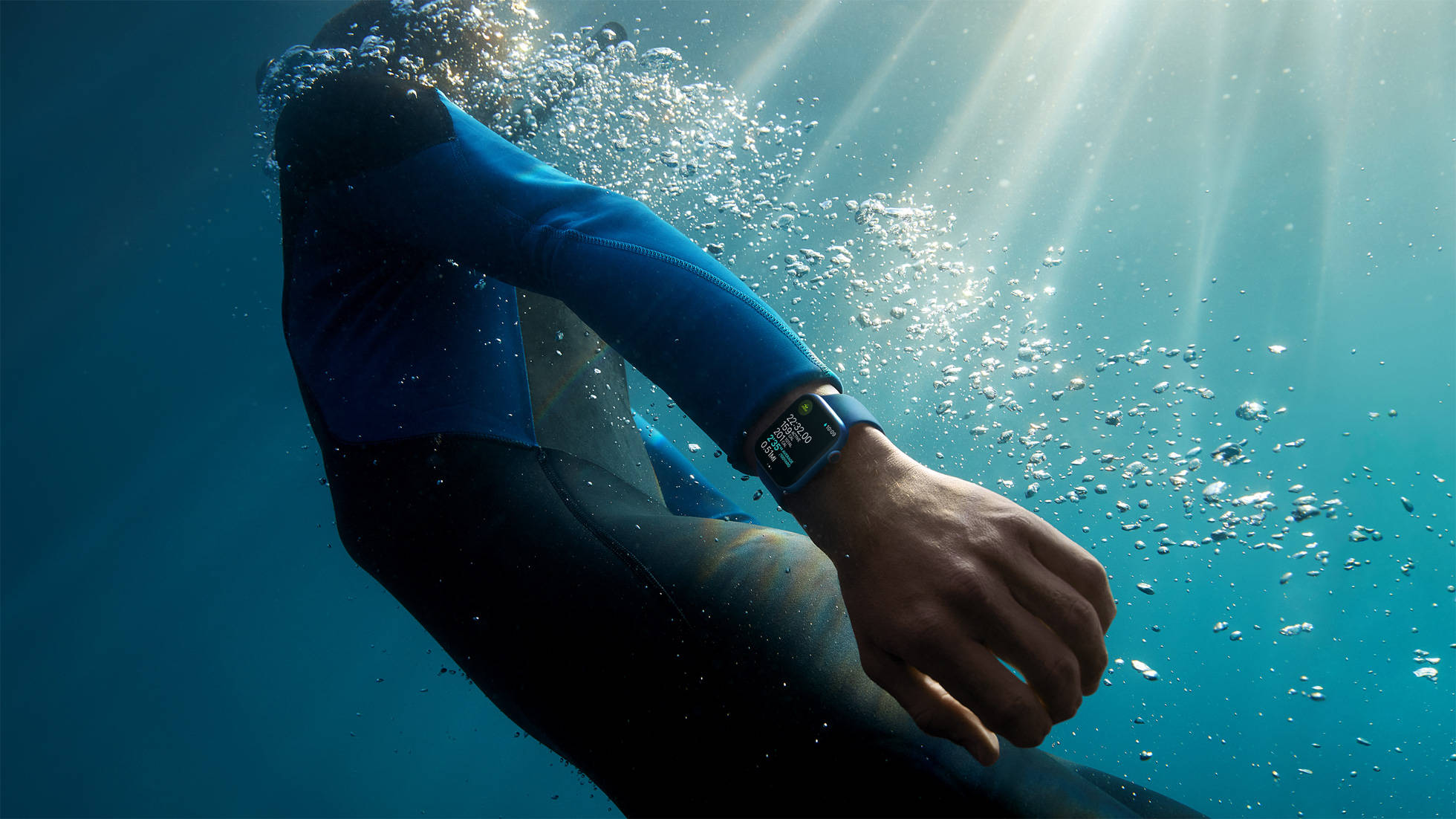 Apple Watch 動態 桌布 壁紙 — 一名穿著藍色潛水衣的潛水員在水下游泳，陽光穿過清澈的藍色海水照射下來，在氣泡周圍產生閃閃發光的效果。