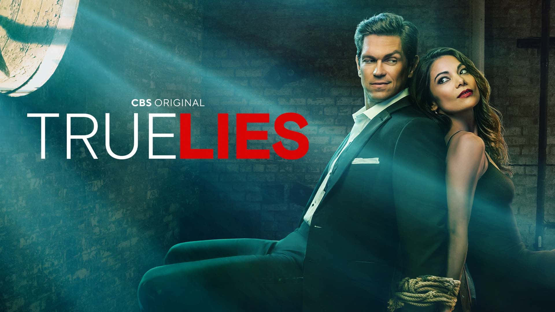 True Lies 桌布 壁紙 — 一名穿著西裝的男子和一名穿著連衣裙的女子在光線昏暗的磚房裡背靠背站立，戲劇性的燈光下，標題《True Lies》顯眼地展示。