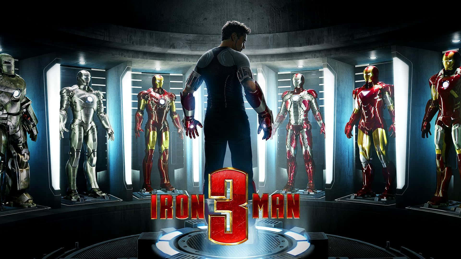 Iron Man Suit 桌布 壁紙 — 一名穿著西裝的男子站在一個高科技實驗室中，面前是圓形展示的多種鋼鐵人戰衣，周圍有發光的燈光。