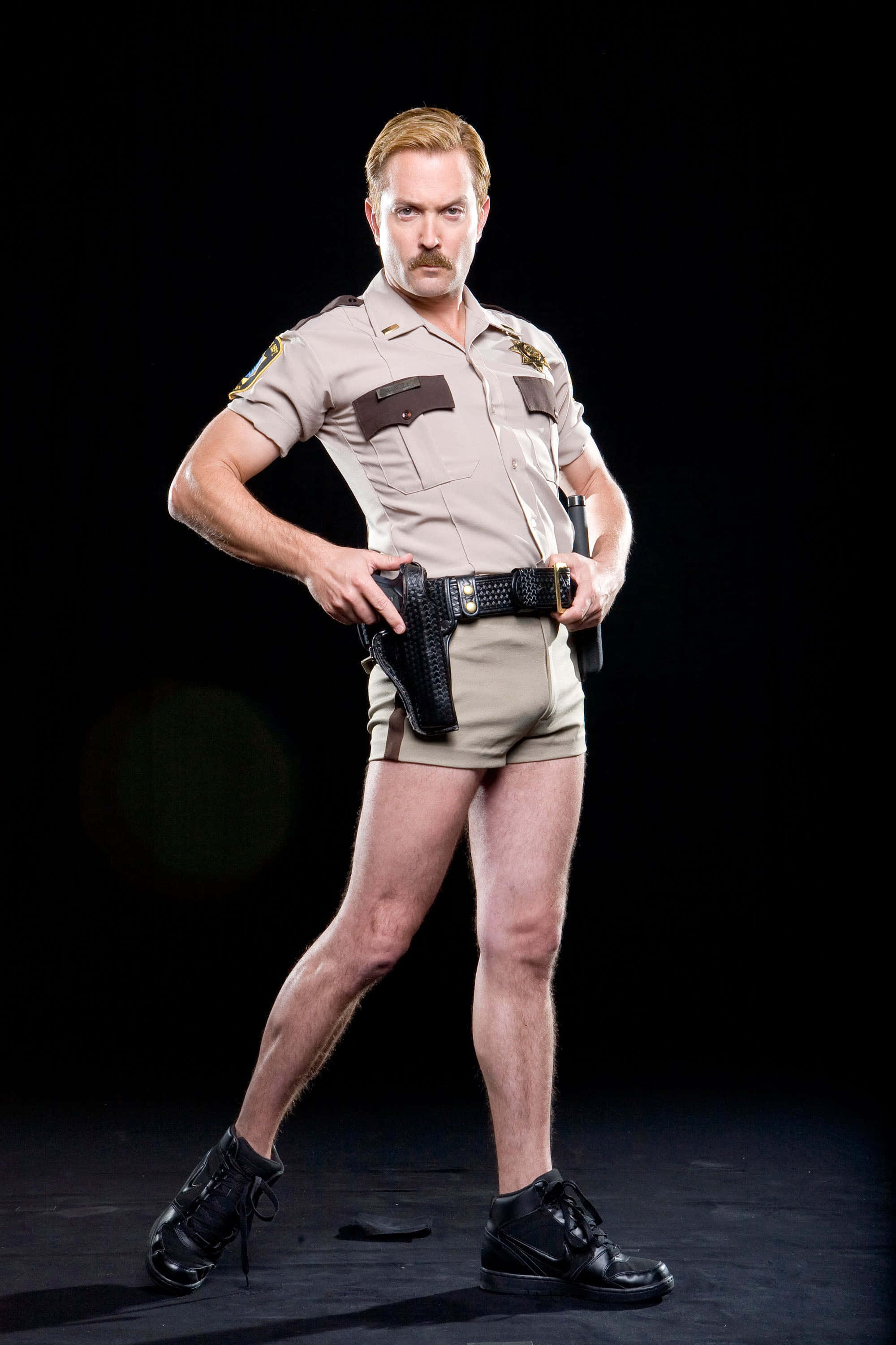thomas lennon 桌布 壁紙 — 一名穿著警長制服、短褲和靴子的男子在黑色背景前自信地擺姿勢。