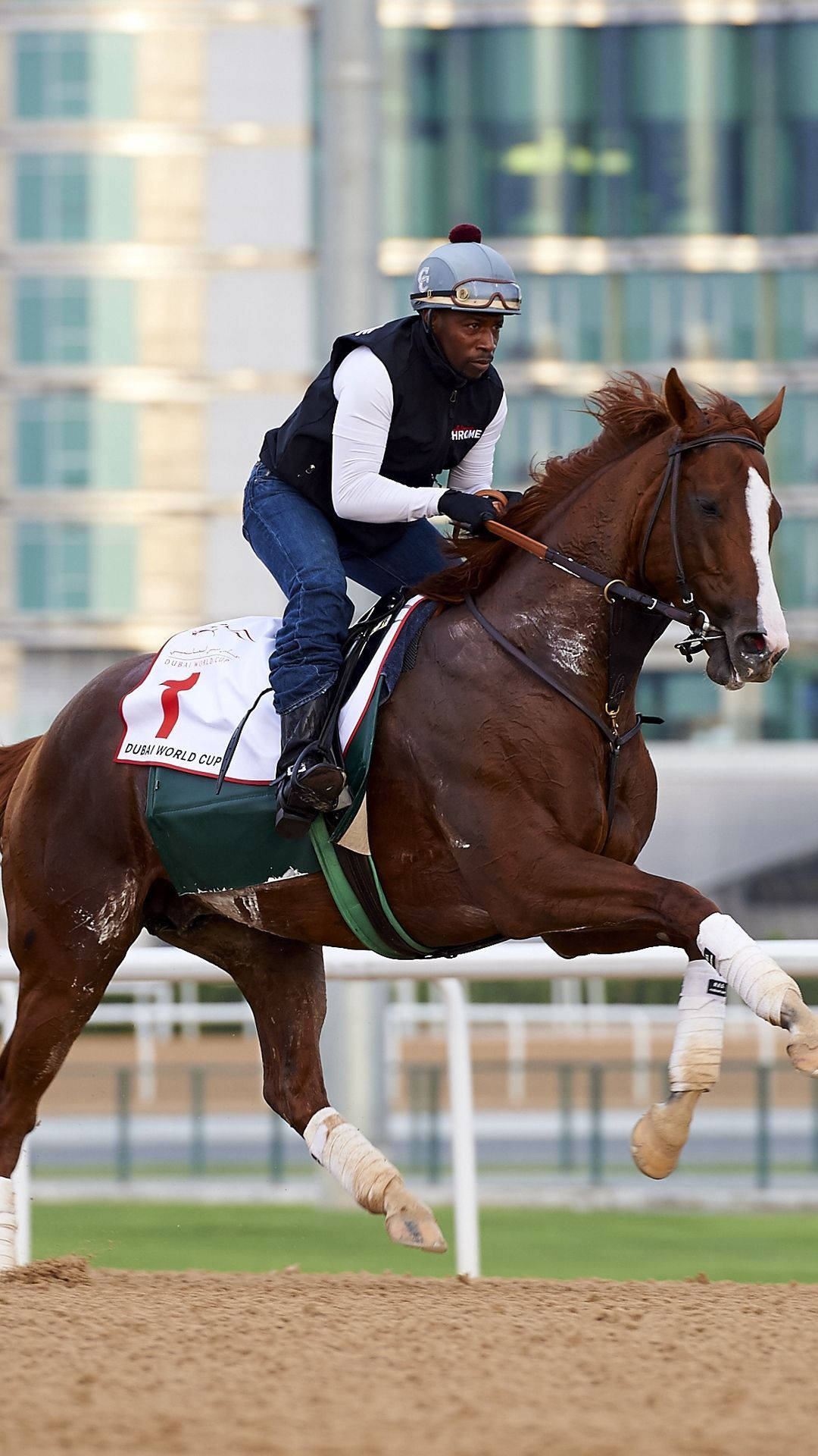 Horse Racing 桌布 壁紙 — 一名穿著賽車裝備的騎師向前傾，他強壯的栗色馬在泥地上飛躍，背景有現代建築。