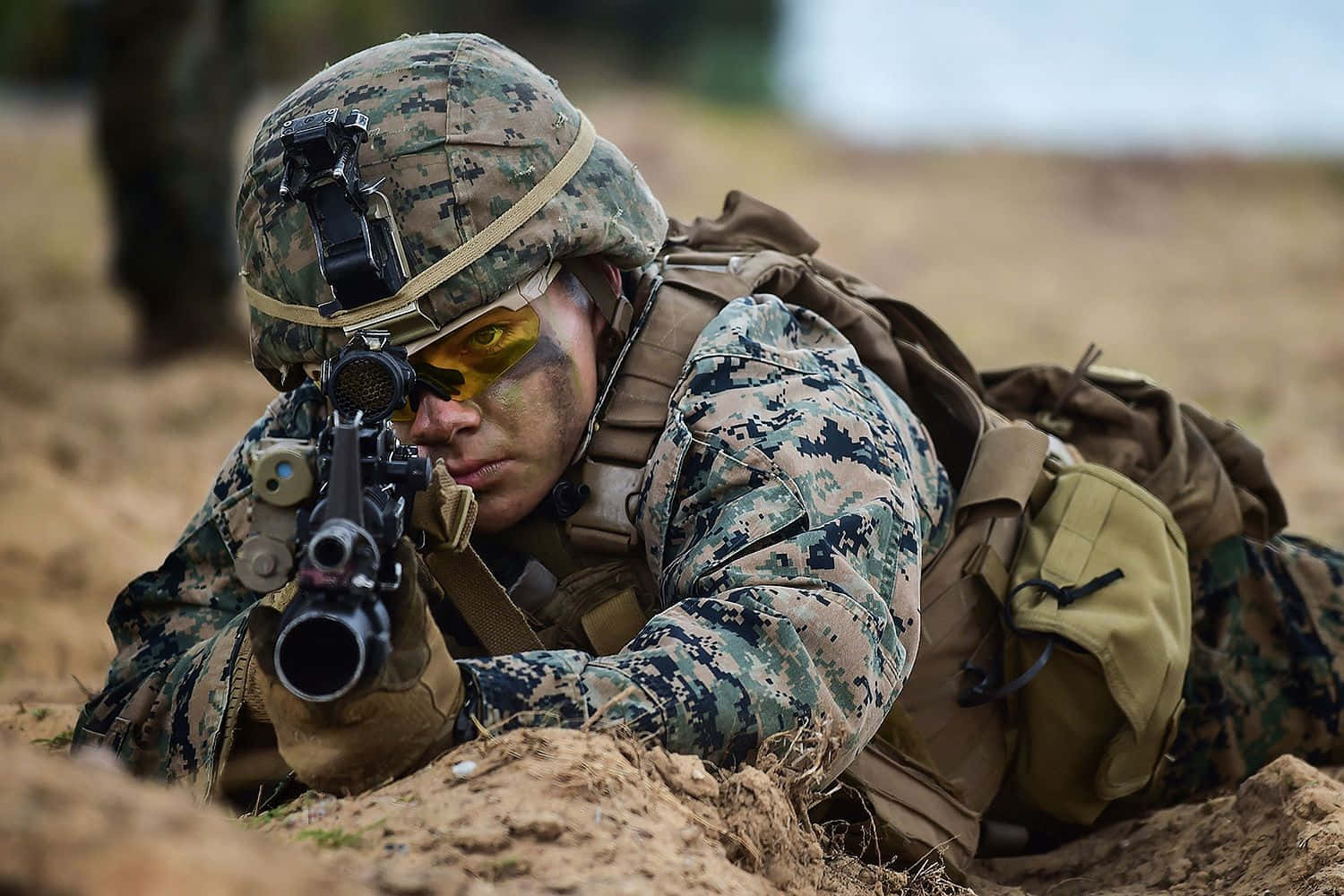 Marines 桌布 壁紙 — 一名穿著迷彩裝備的士兵俯臥在泥地上，專注地瞄準步槍。