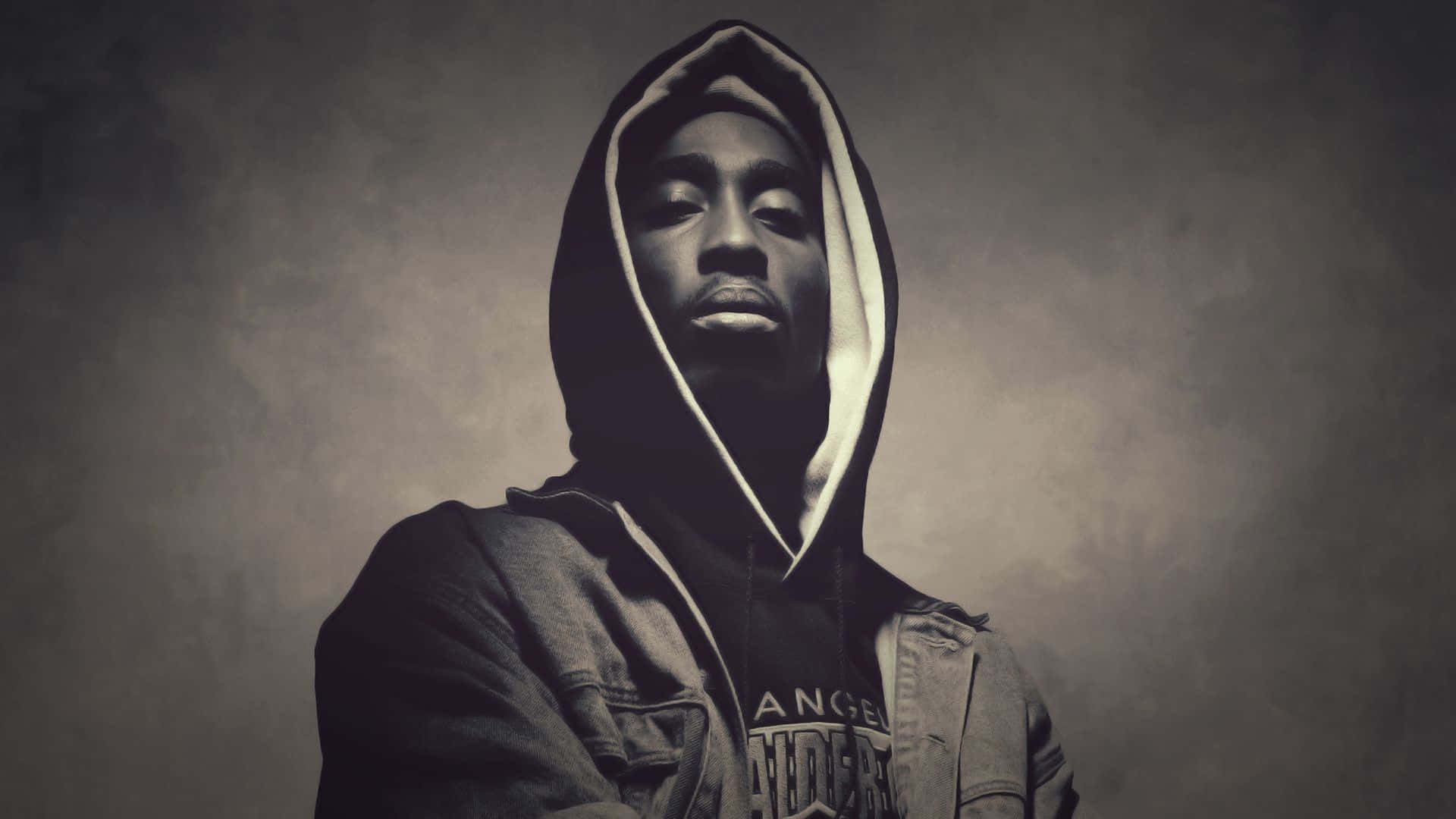 tupac 桌布 壁紙 — 一名穿著連帽衛衣的男子站在煙灰色背景前，表情嚴肅。