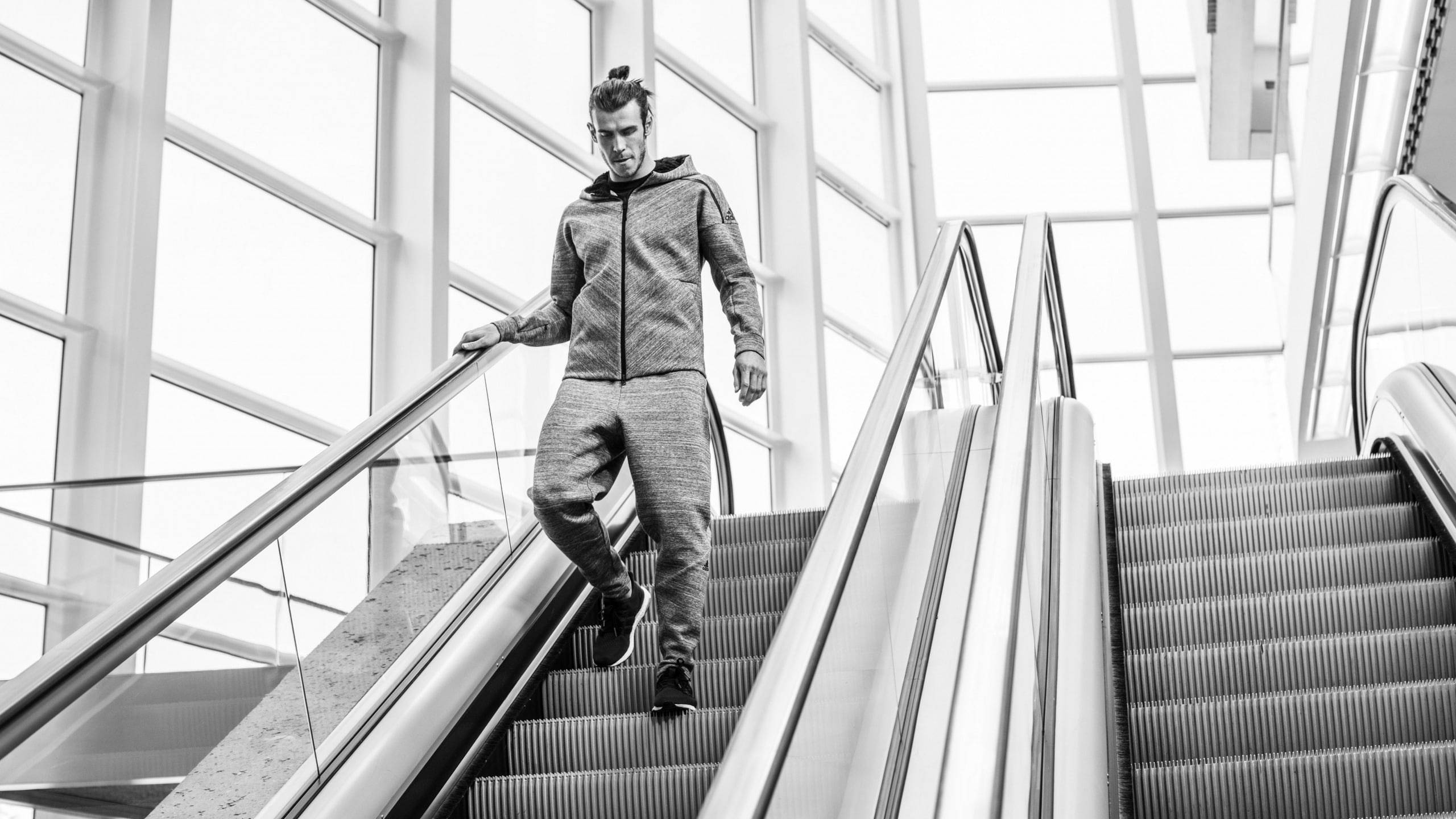 Gareth Bale 桌布 壁紙 — 一名穿著運動服的男子在單色調中，走下一條由大窗戶框著的現代化自動扶梯。