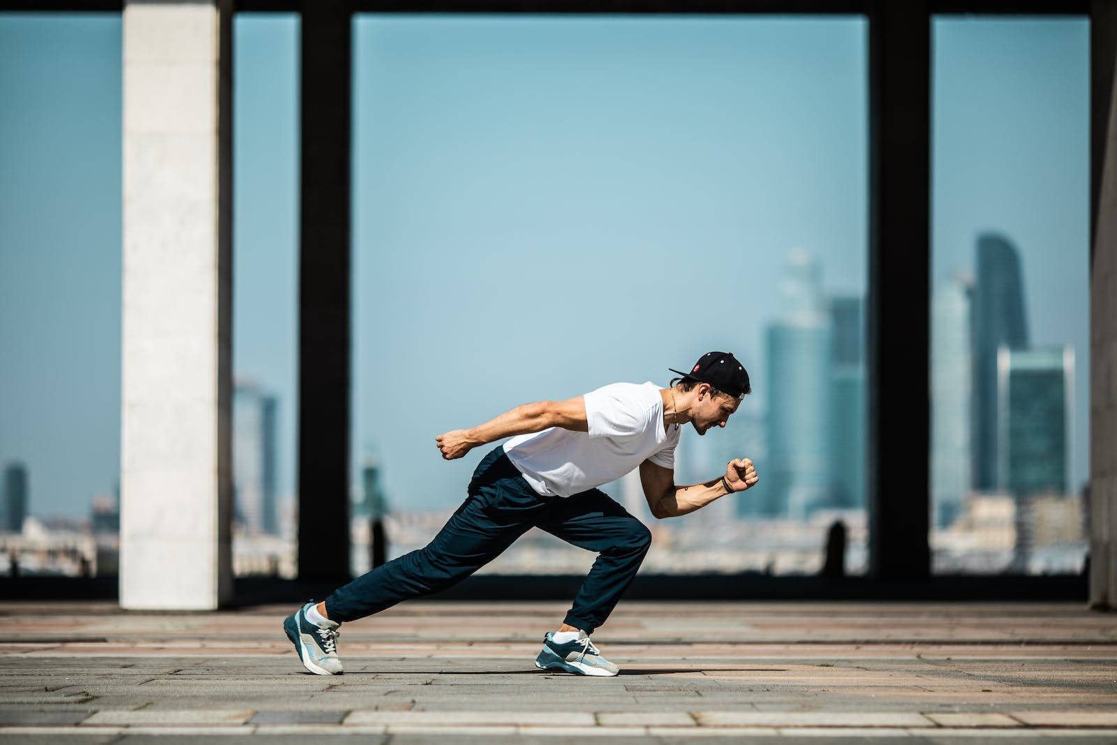 Motivation 桌布 壁紙 — 一名穿著運動服的男子在瓷磚廣場上動態伸展，身後的大型玻璃面板可見現代城市天際線。
