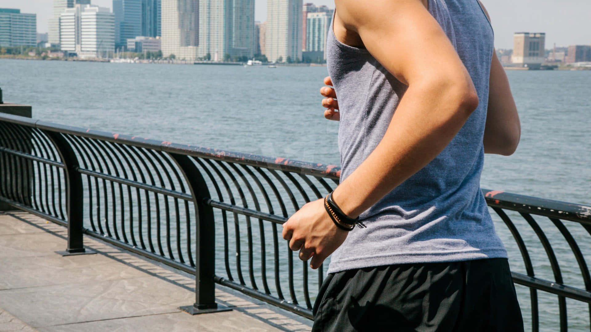 Workout 桌布 壁紙 — 一名穿著運動服的男子沿著海濱長廊跑步，身後是城市天際線和寧靜的水面。