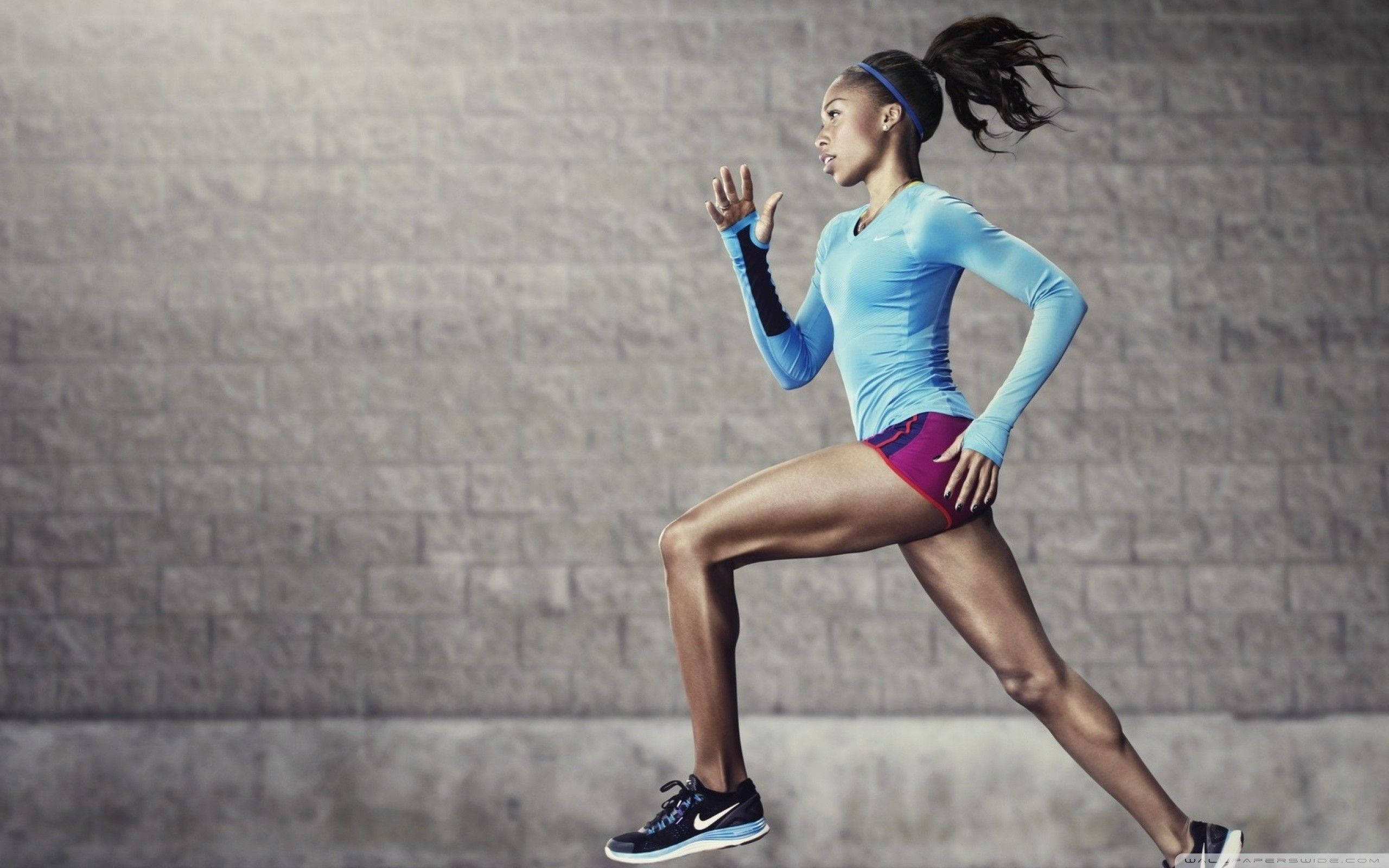 Marathon 桌布 壁紙 — 一名穿著運動裝備的女性，動態地衝刺在帶有紋理的灰色磚牆前，頭髮因動作而模糊。