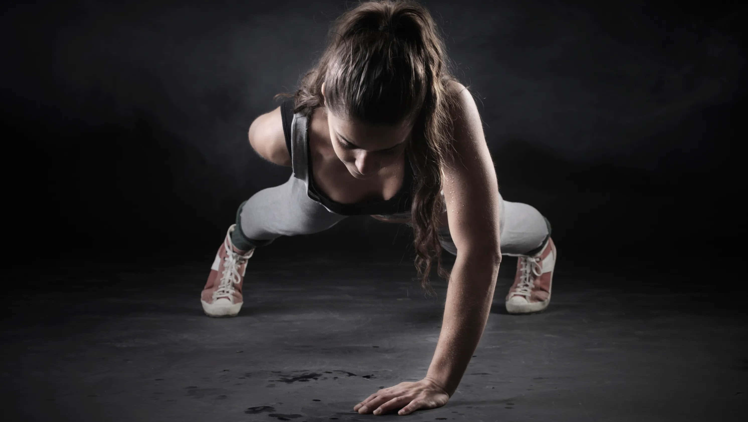 Fitness 桌布 壁紙 — 一名穿著運動裝備的女性在煙霧瀰漫的黑暗工作室背景下做出動態的伏地挺身姿勢。