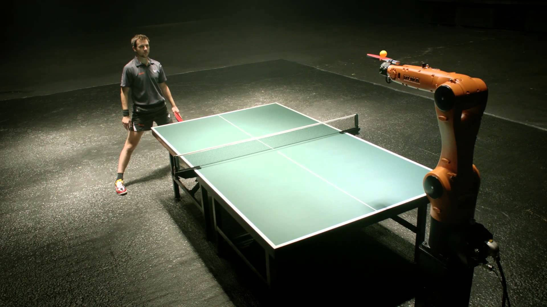 Table Tennis 桌布 壁紙 — 一名穿著運動裝備的男子準備在昏暗的工業空間中，與一個拿著球的橙色機械臂打乒乓球。