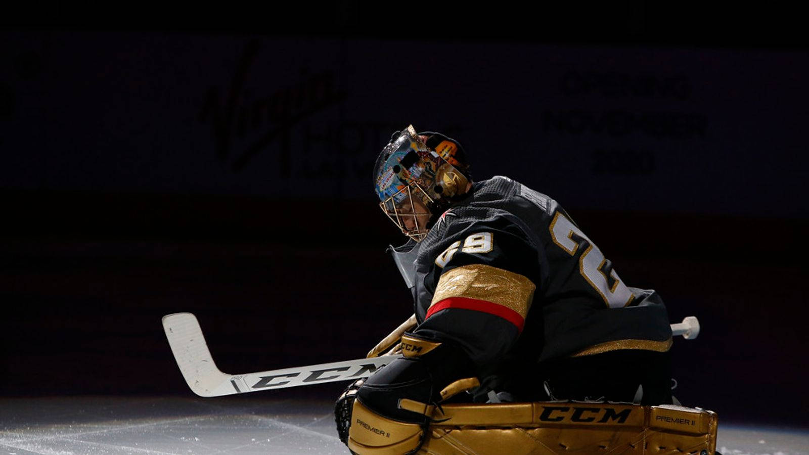 hockey 桌布 壁紙 — 一名穿著金色和黑色裝備的冰球守門員在場館燈光下低蹲在冰上，手持球桿。