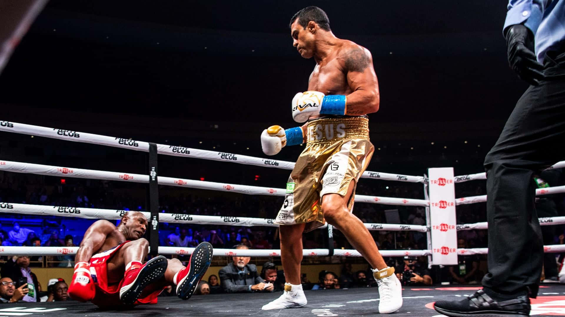Boxing 桌布 壁紙 — 一名穿著金色短褲的拳擊手在燈光明亮的擂台上戰勝倒下的對手，裁判在附近。