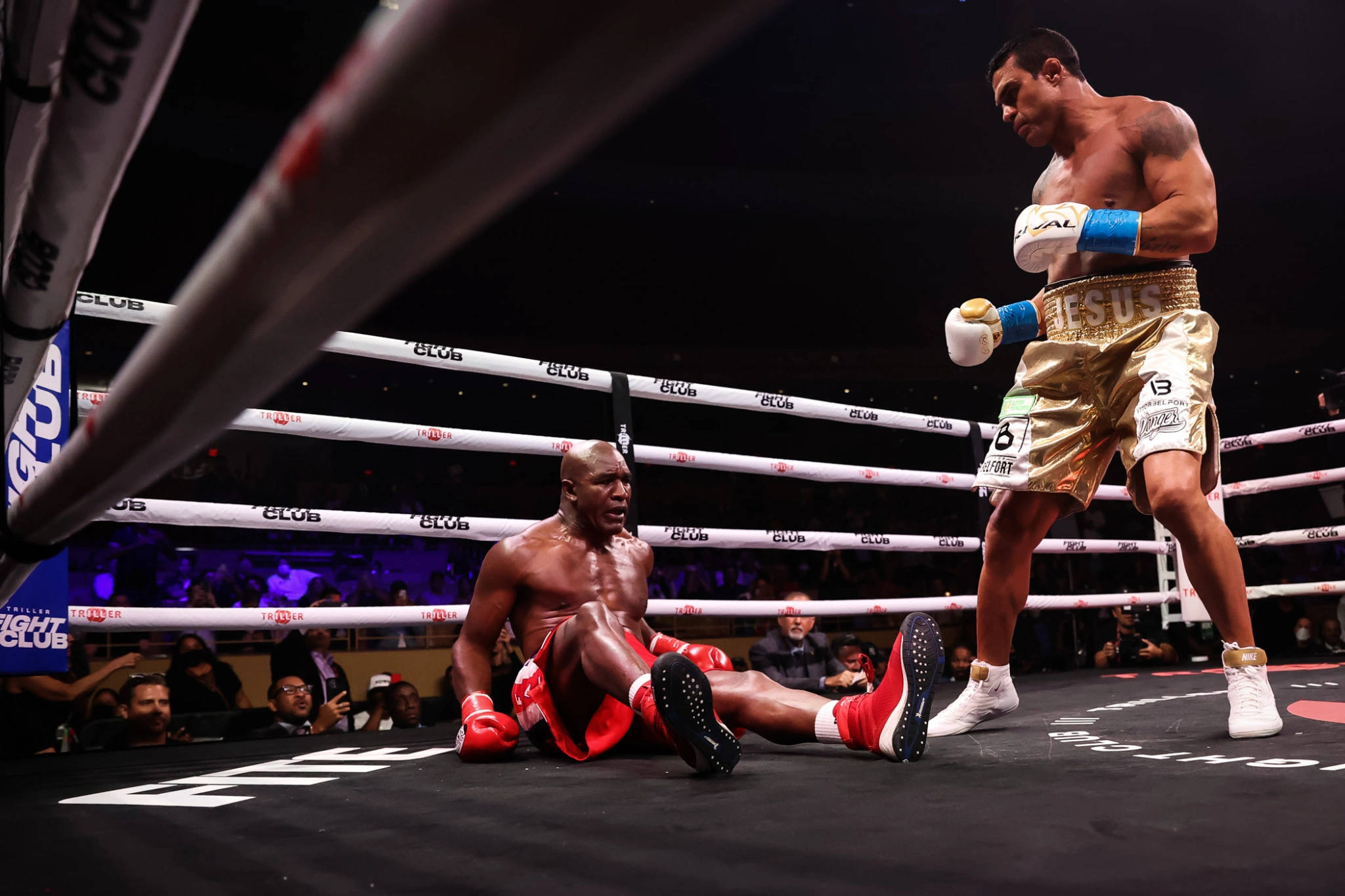 Boxing 桌布 壁紙 — 一名穿著金色短褲的拳擊手在燈光昏暗的擂台上，勝利地站在倒下的對手之上，觀眾咆哮。
