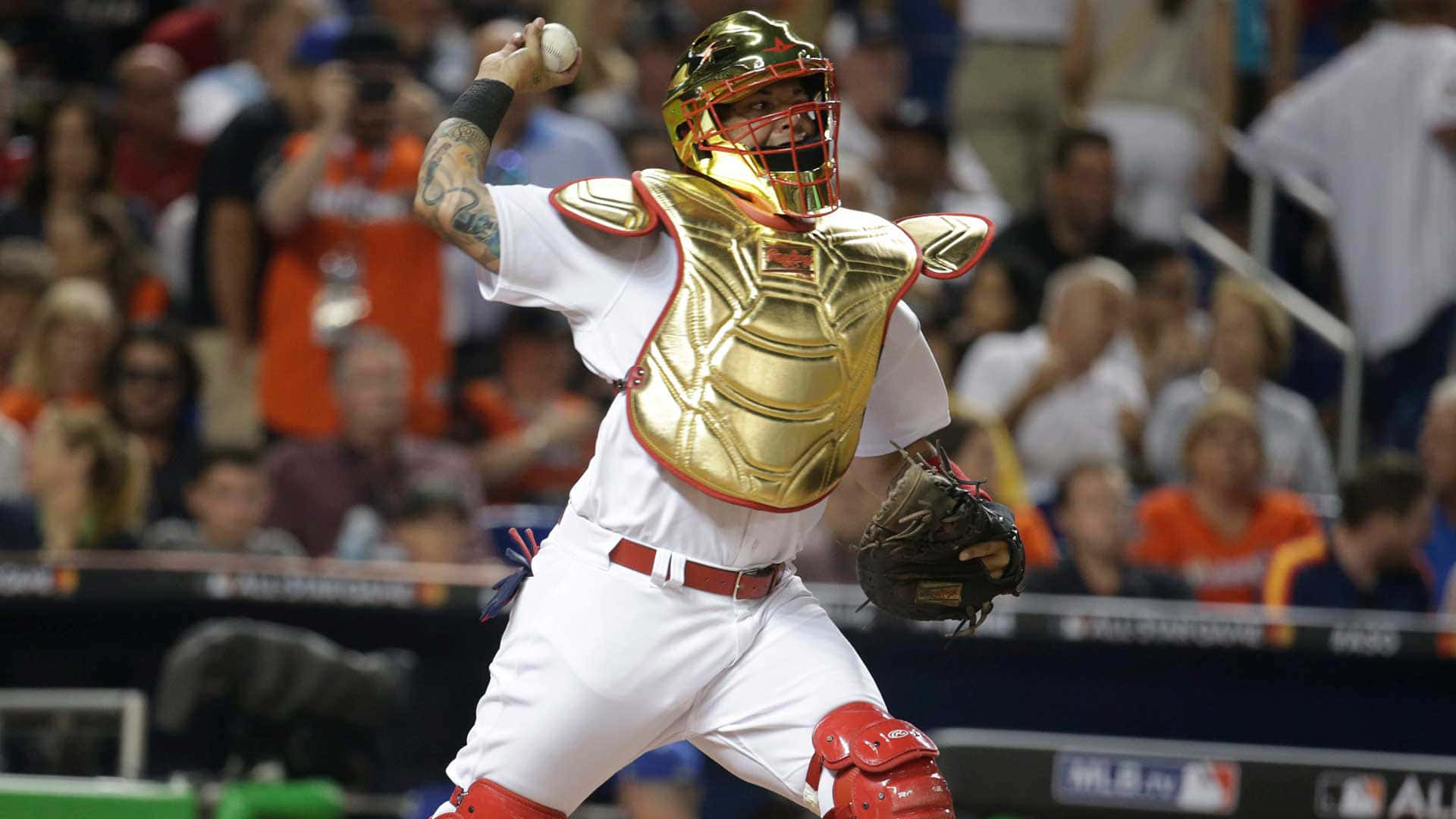 Yadier Molina 桌布 壁紙 — 一名穿著金色護胸和紅色裝備的棒球捕手在背景有觀眾的情況下，於動作中投球。