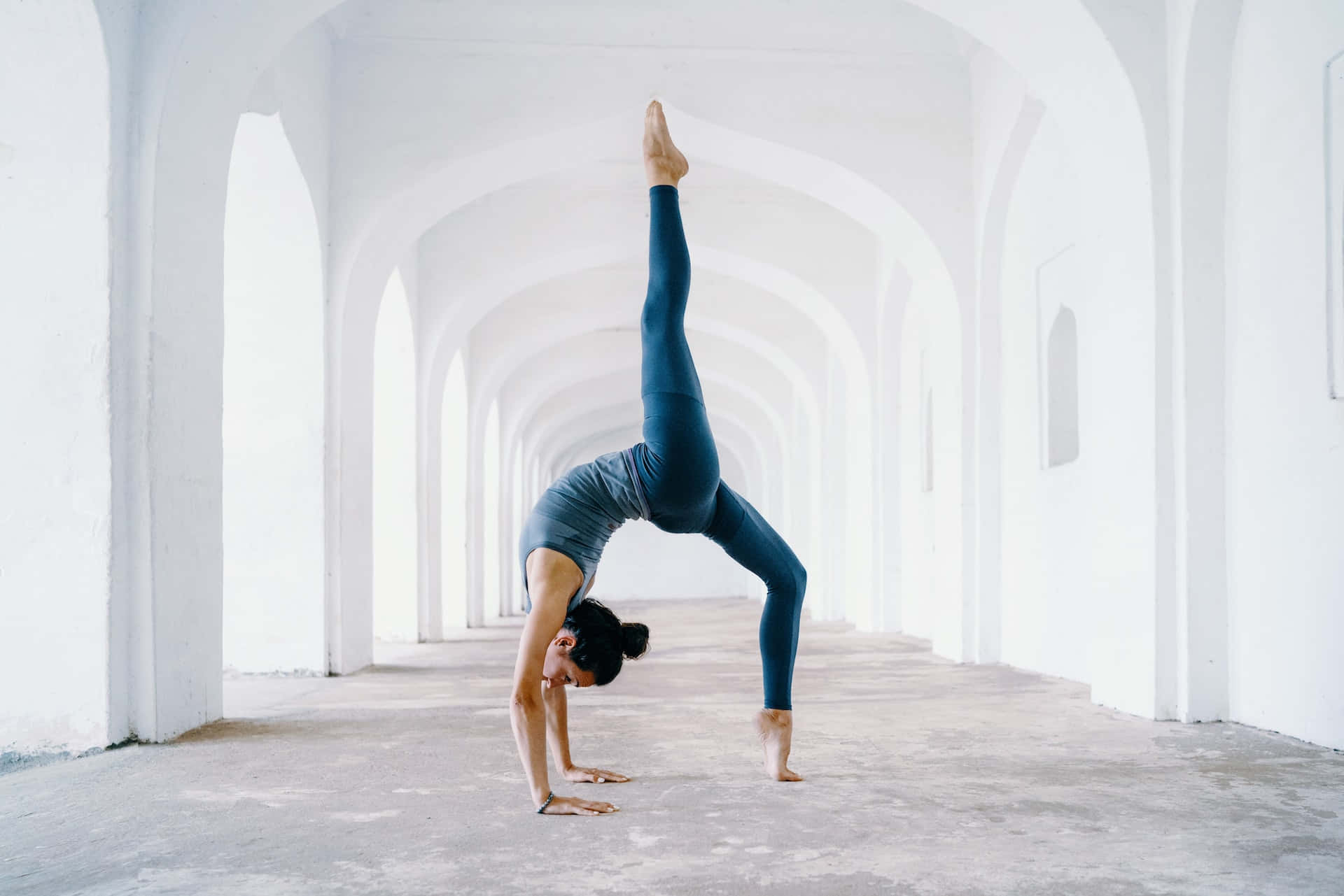 Exercise 桌布 壁紙 — 一名穿著青綠色緊身褲的女性在長長的白色拱形走廊中做倒立，其中一條腿伸直。