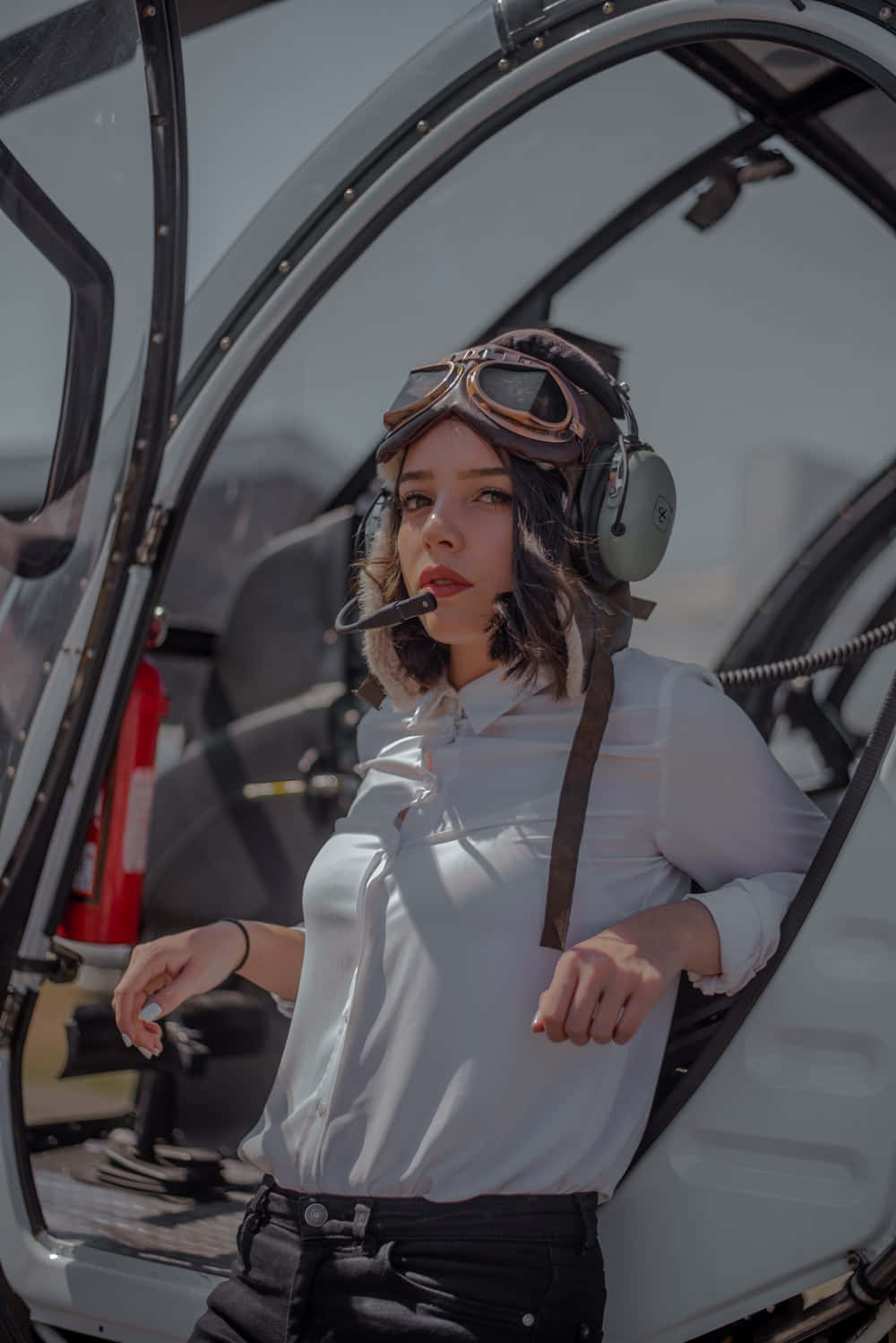 Plane 桌布 壁紙 — 一名穿著飛行員裝備的女性在明亮的日光下自信地站在直升機駕駛艙的敞開門中。