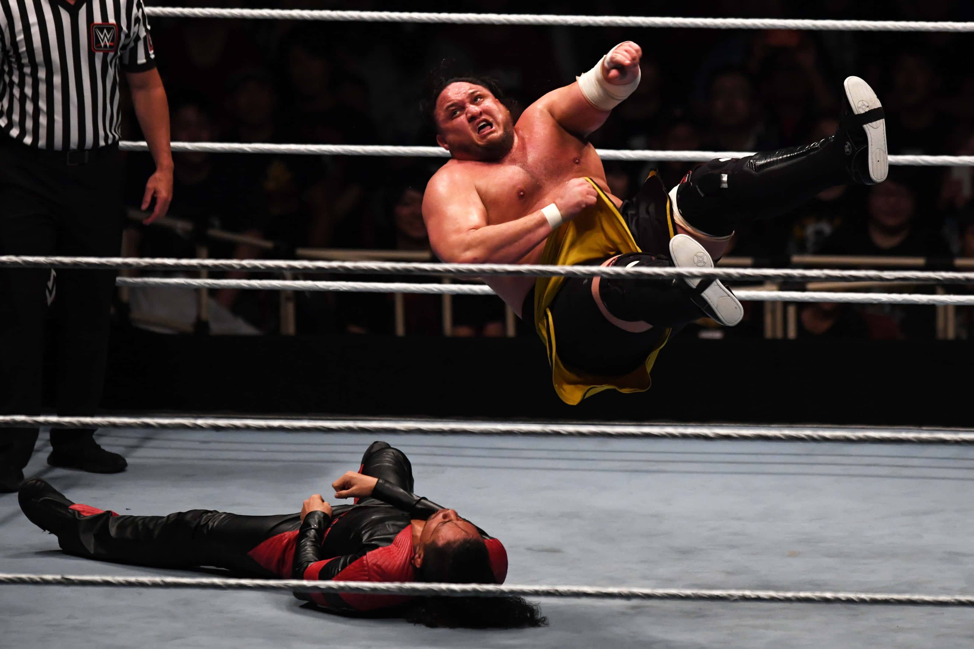 WWE 桌布 壁紙 — 一名穿著黃色短褲的摔角手在空中躍向摔角場內躺在墊子上的對手。