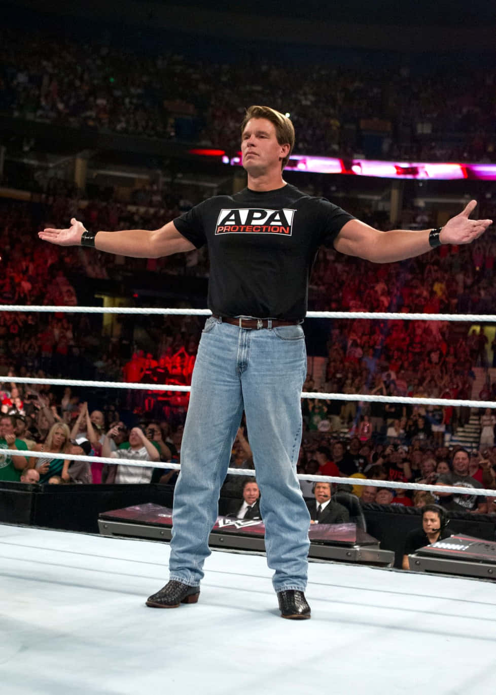 WWE 桌布 壁紙 — 一名穿著黑色APA Protection T恤和牛仔褲的摔角手，在燈光明亮的擂台上張開雙臂，面對著歡呼的人群。