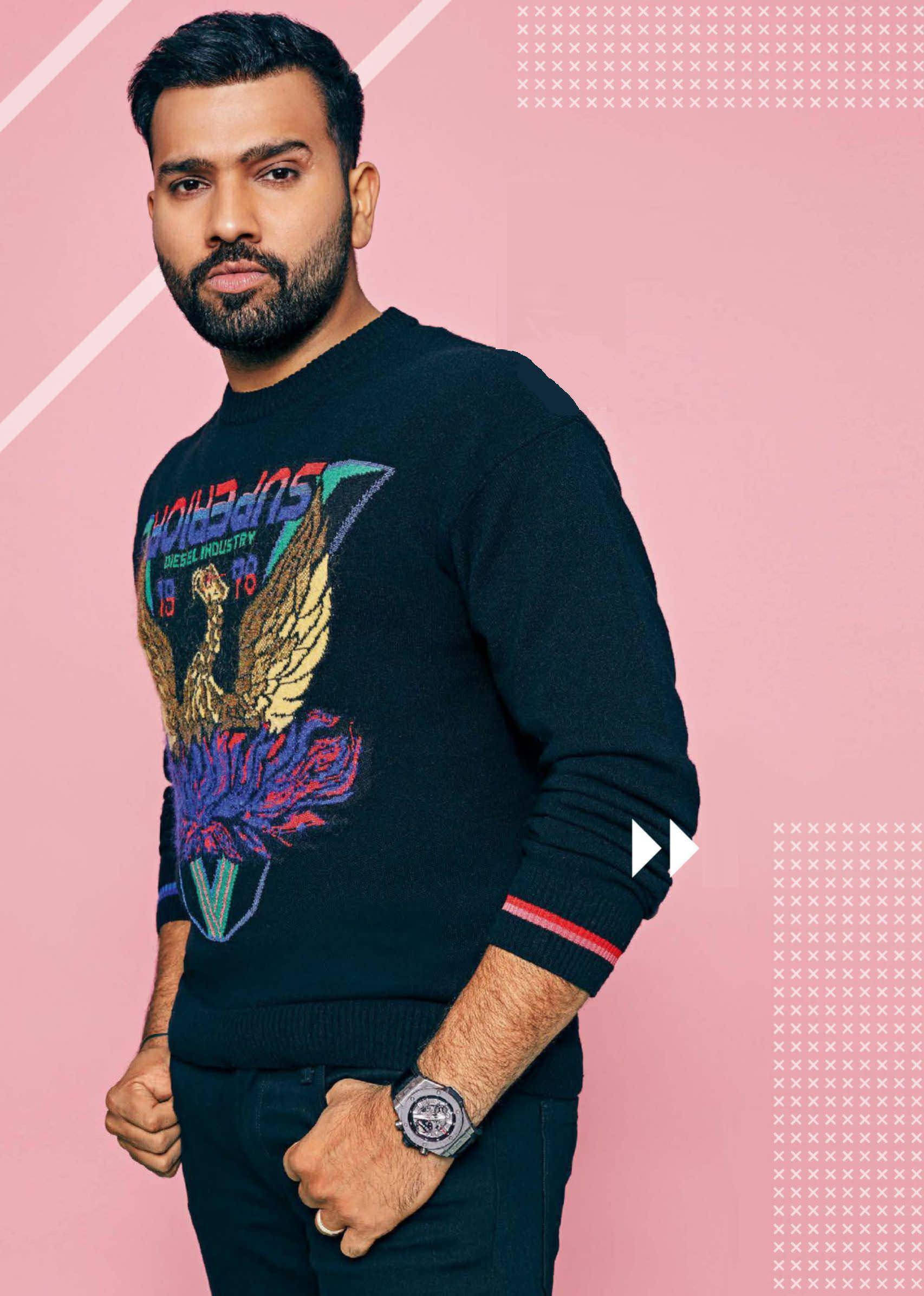 Rohit Sharma 桌布 壁紙 — 一名穿著黑色毛衣、帶有彩色鷹圖案的男人，自信地站在粉紅色幾何背景前。
