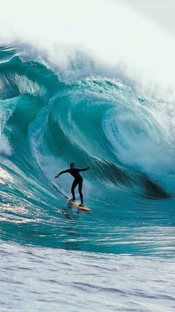 Surfing iPhone 桌布 壁紙 — 一名穿著黑色潛水衣的衝浪者騎乘著巨大的藍綠色海浪，頭頂有白色泡沫翻騰。