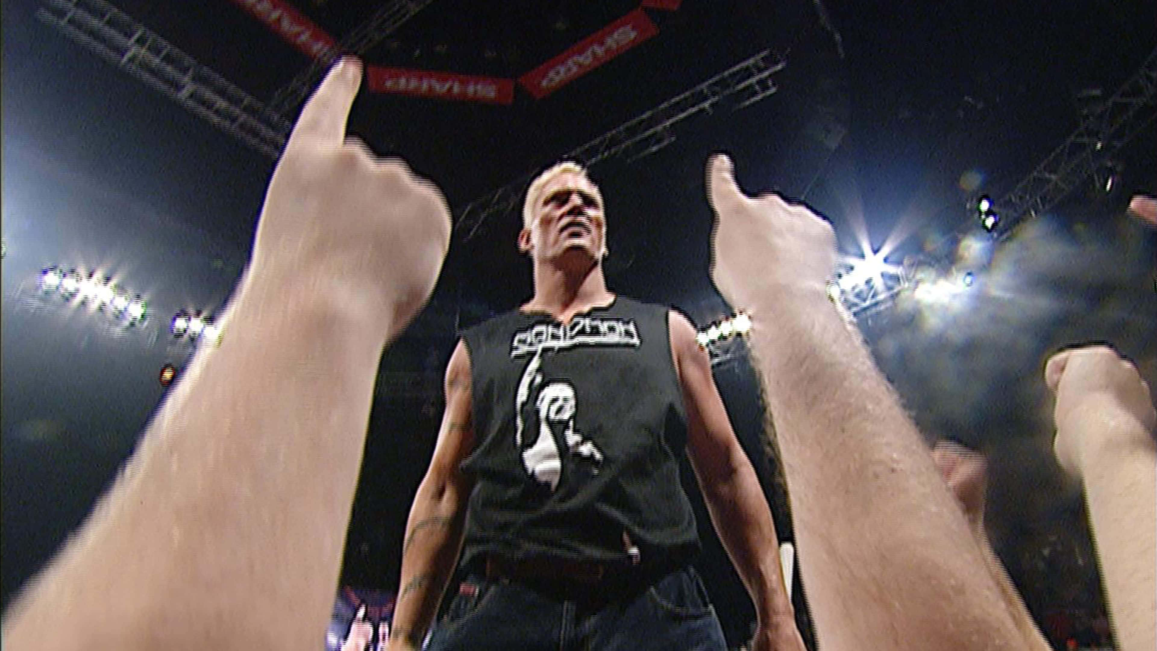 WWE 桌布 壁紙 — 一名穿著黑色背心的摔角手站在明亮的競技場燈光下中央，粉絲們舉起大拇指。
