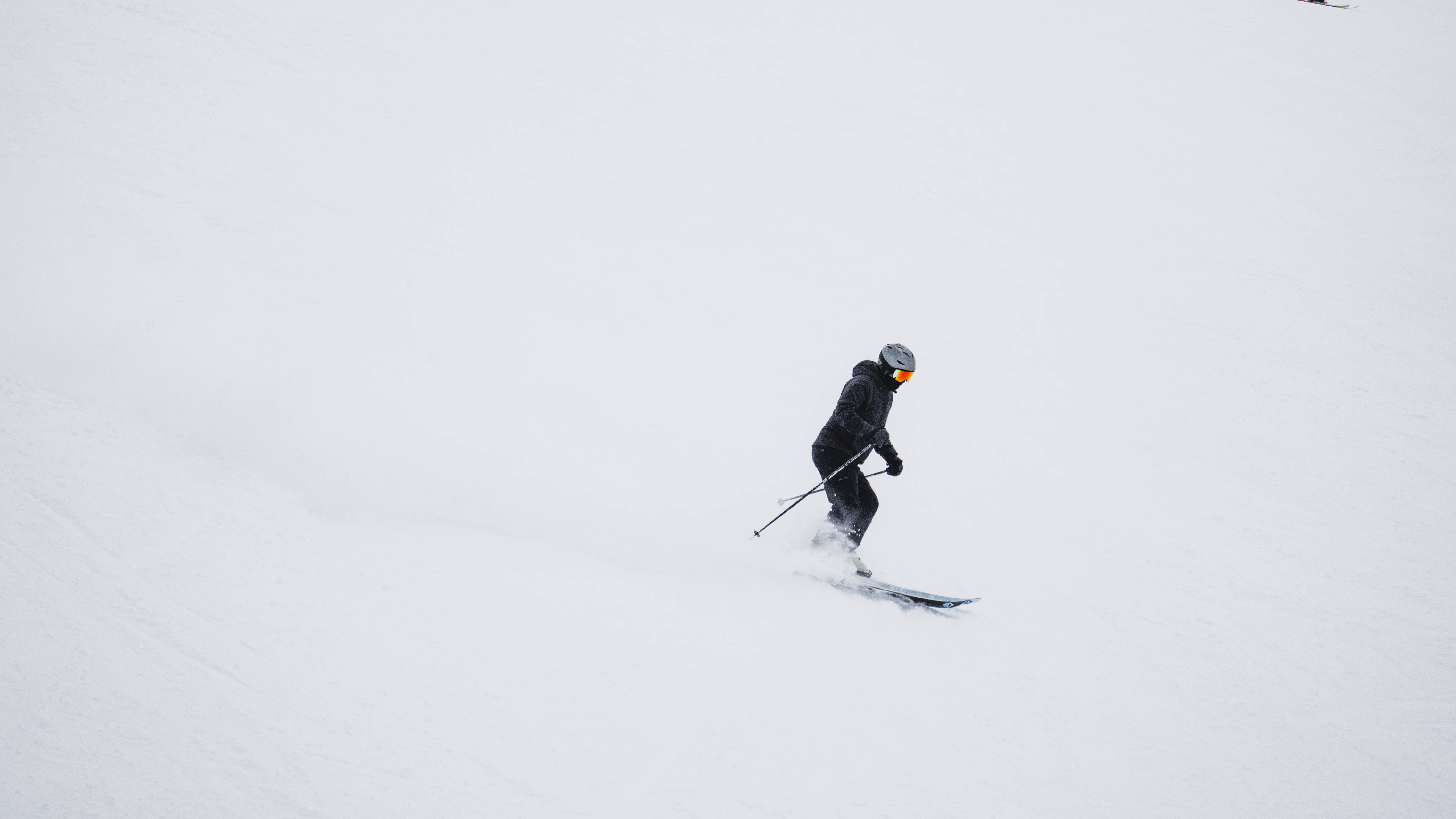 滑雪 桌布 壁紙 — 一名穿著黑色裝備的滑雪者在多雲的天空下，在廣闊的雪坡上劃過新鮮的粉雪。