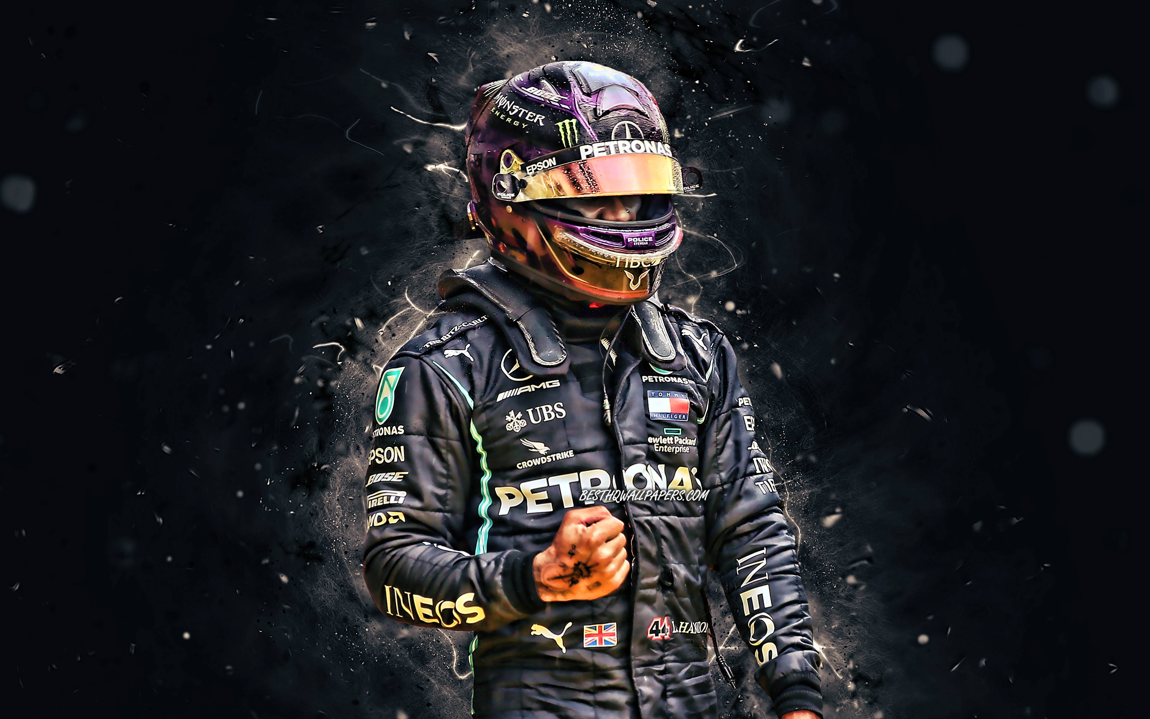 Hamilton F1 桌布 壁紙 — 一名穿著黑色賽車服和頭盔的F1車手站在黑暗背景前，周圍有發光粒子旋轉。