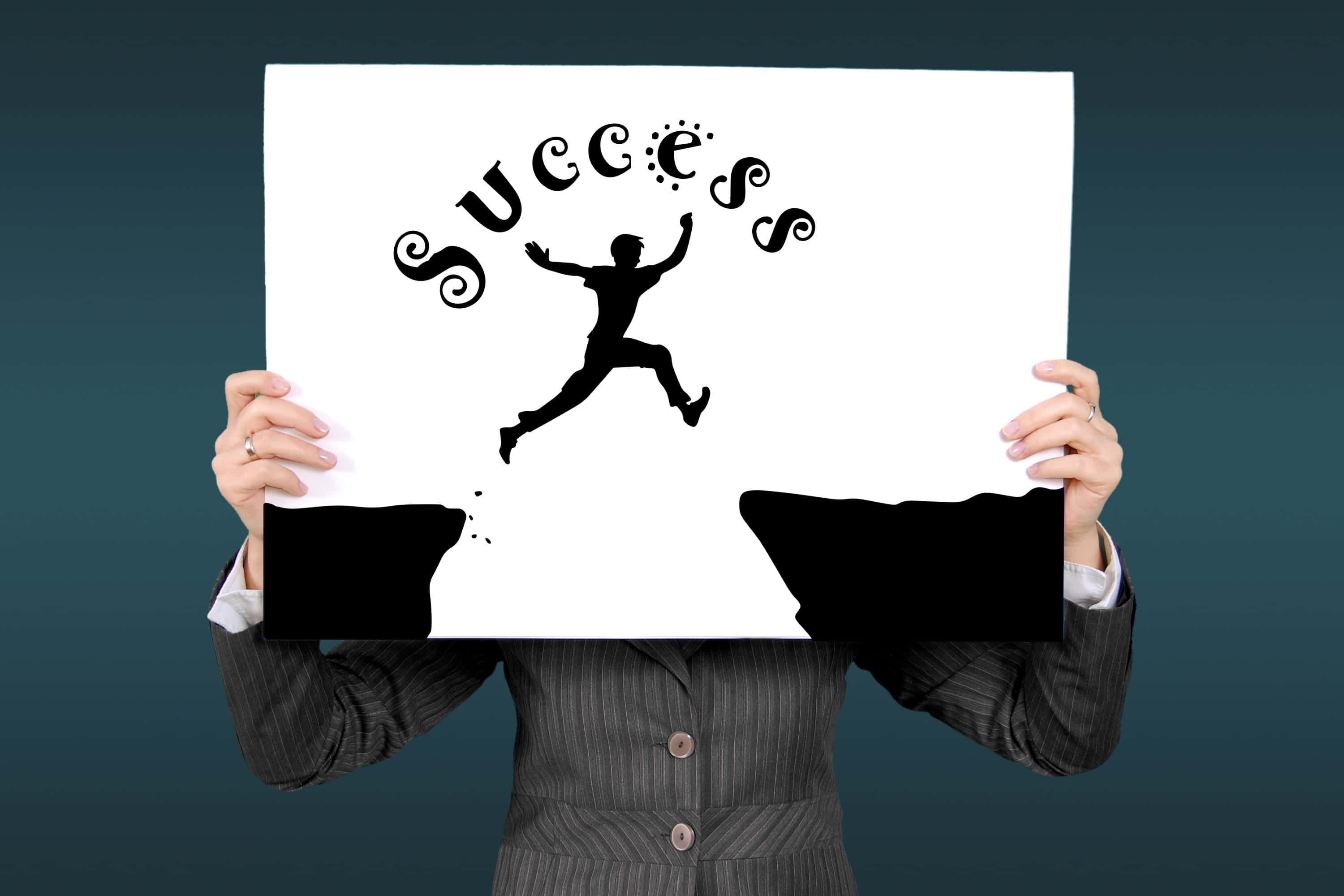 Success 桌布 壁紙 — 一名穿西裝的人手持一個白色標牌，上面有黑色剪影的跳躍人物，上方拱形寫著 success 一詞。