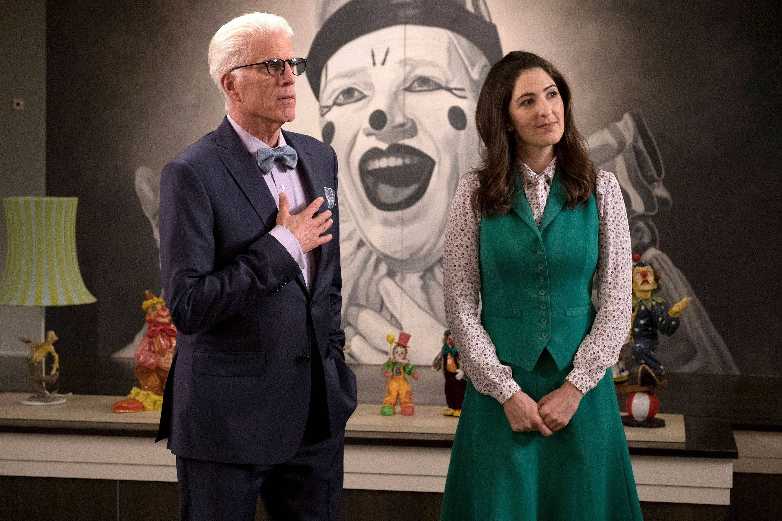 Netflix 桌布 壁紙 — 一名穿西裝的男子和一名穿綠色連衣裙的女子站在一個充滿彩色公仔的房間裡，面前是一幅大型小丑肖像。