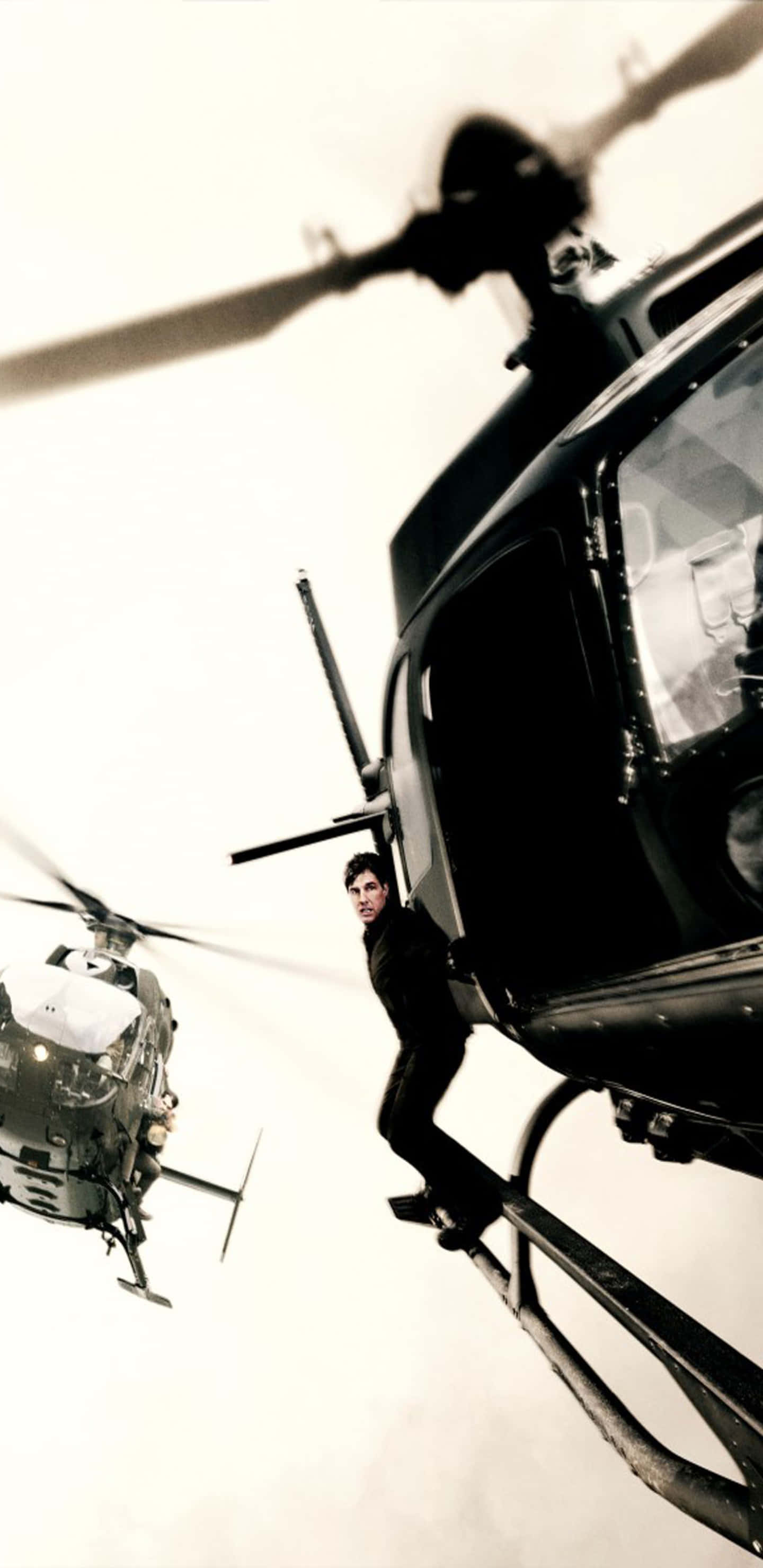 Helicopter 桌布 壁紙 — 一名穿黑衣的男子懸掛在直升機旋翼槳葉上，背景是明亮的白色天空，附近有另一架直升機。