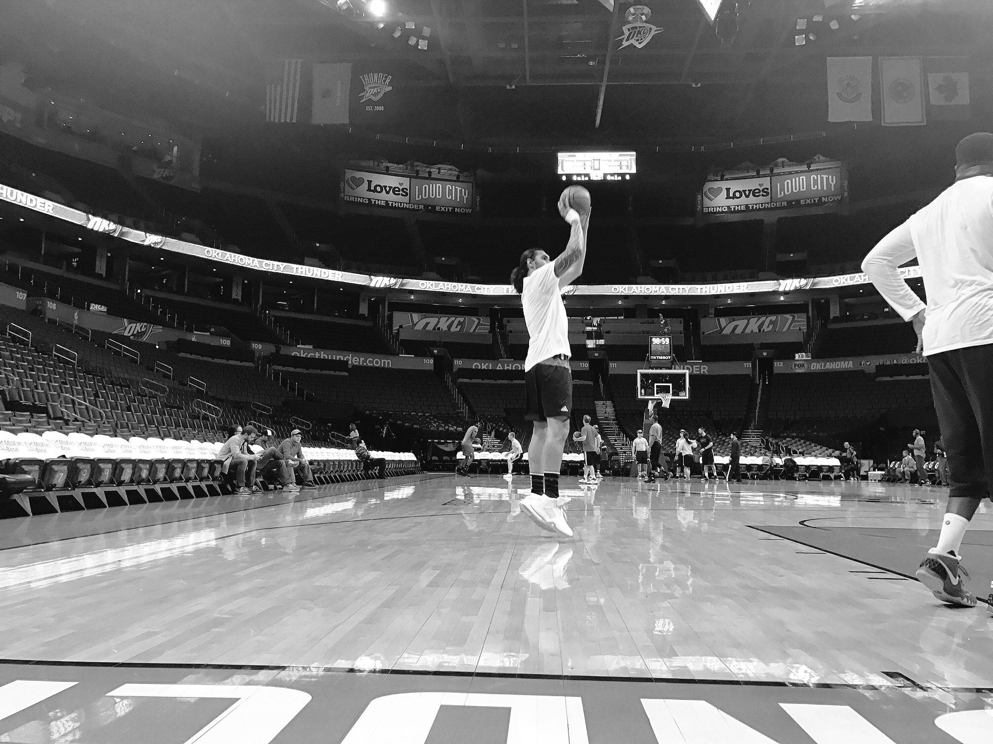 Steven Adams 桌布 壁紙 — 一名籃球運動員在單色調的球場上跳起投罰球，場內座位空無一人，頭頂懸掛著球隊橫幅。