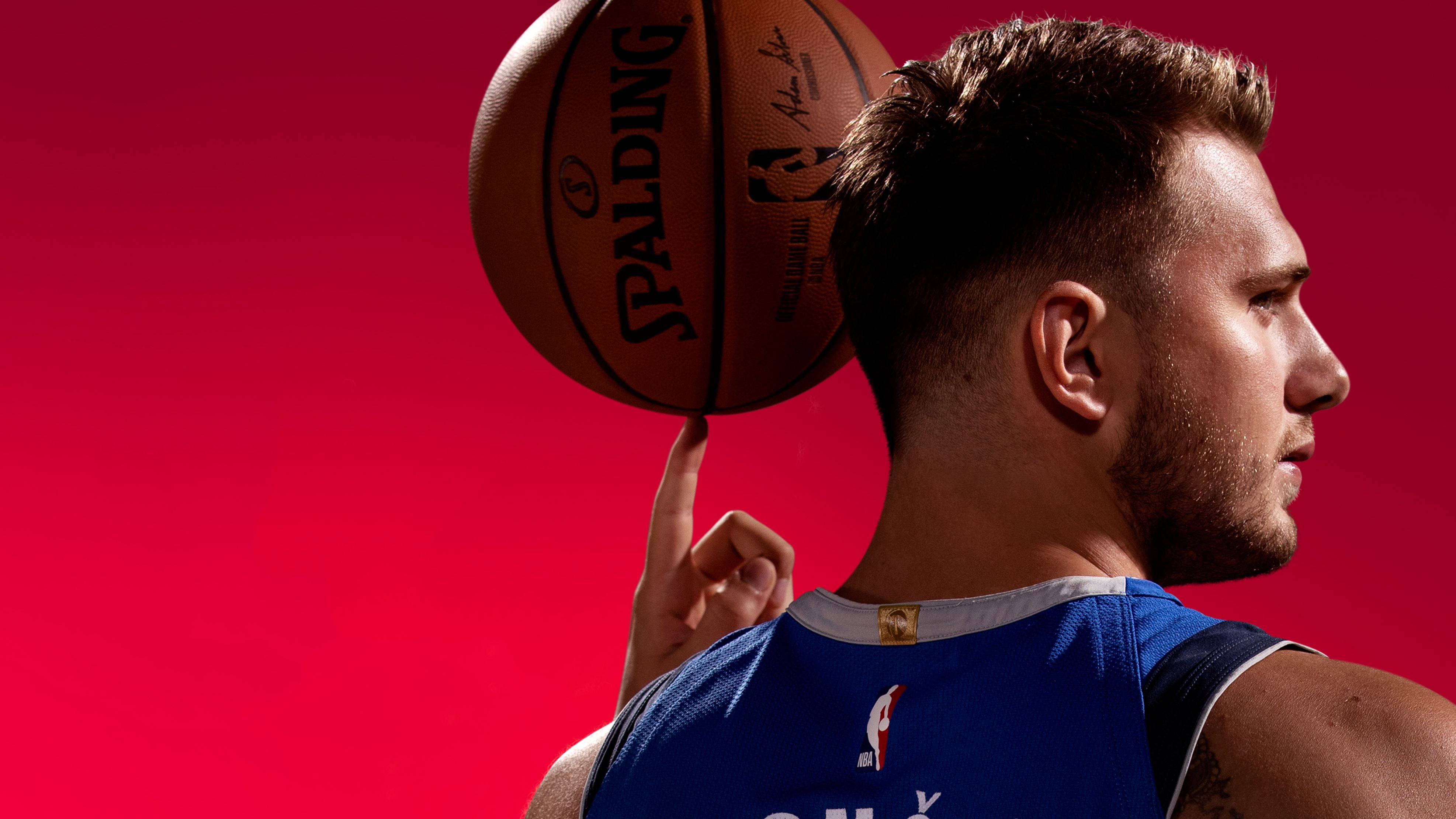 Luka Doncic 桌布 壁紙 — 一名籃球運動員在鮮紅色背景前用指尖平衡 Spalding 籃球。