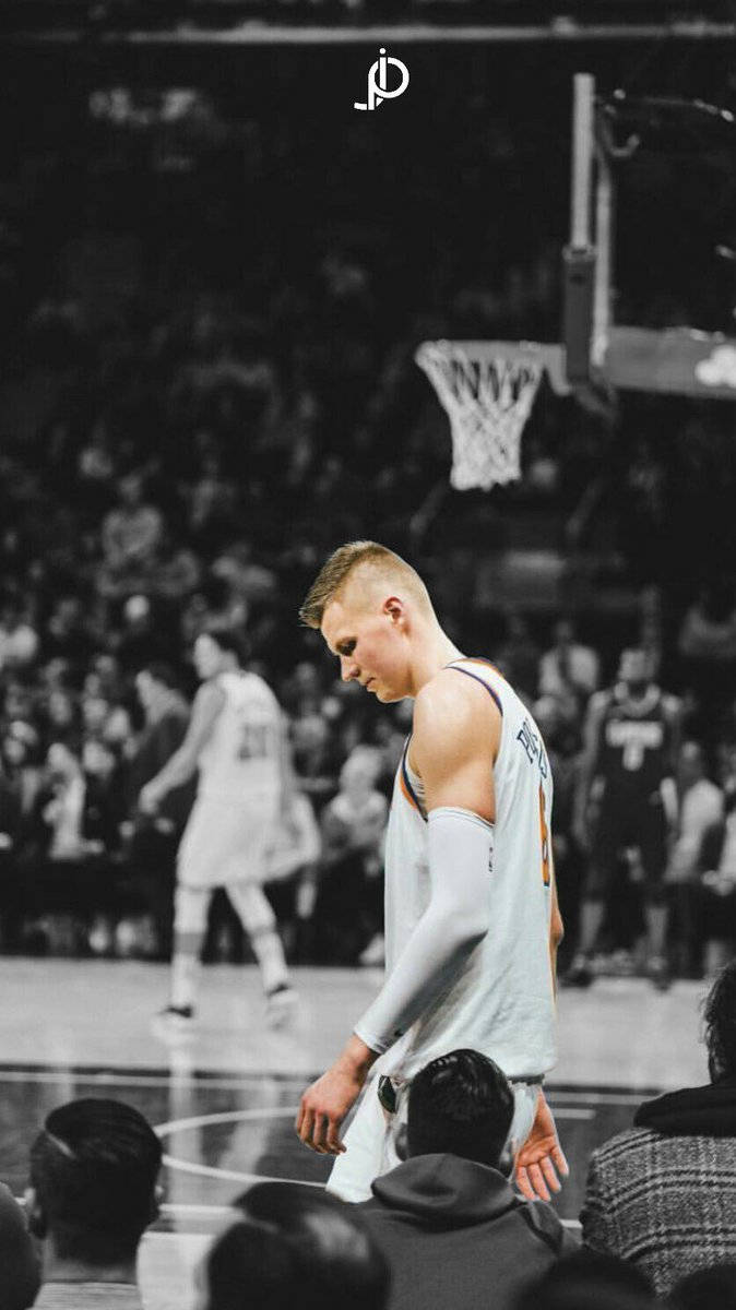 Kristaps Porzingis 桌布 壁紙 — 一名籃球運動員失望地離開球場，黑白畫面，背景有群眾。