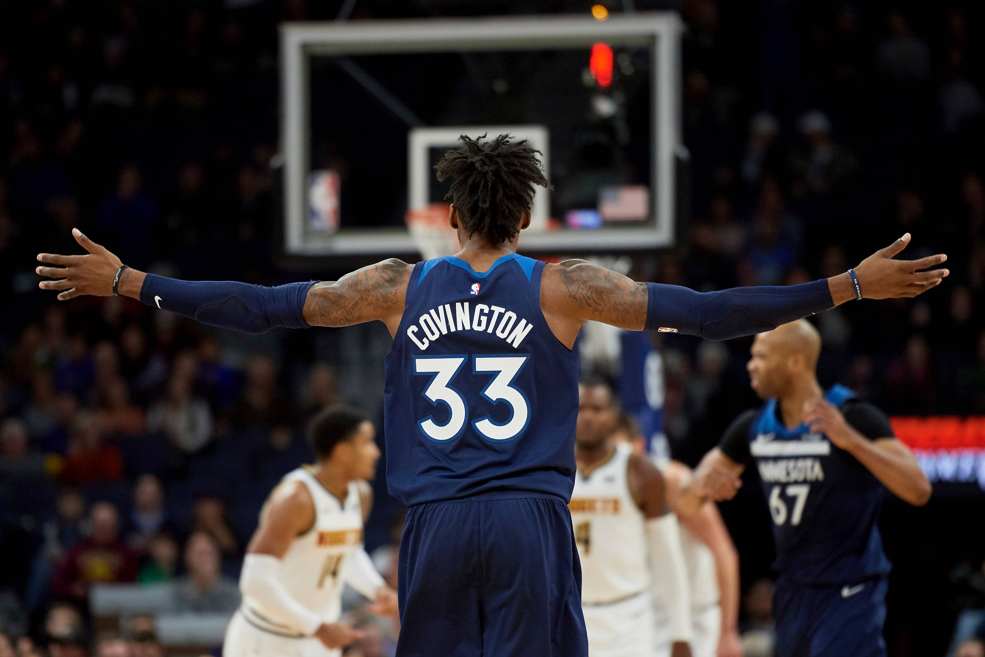 robert covington 桌布 壁紙 — 一名籃球運動員張開雙臂站在球場上，面向籃框，背景中的隊友和人群模糊不清。