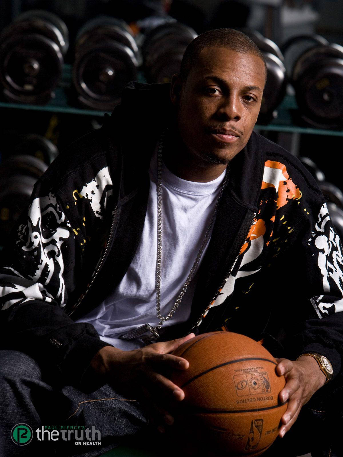 Paul Pierce 桌布 壁紙 — 一名籃球運動員自信地坐著，手持籃球，身後有模糊的健身房槓鈴，營造出陰鬱的攝影棚氛圍。