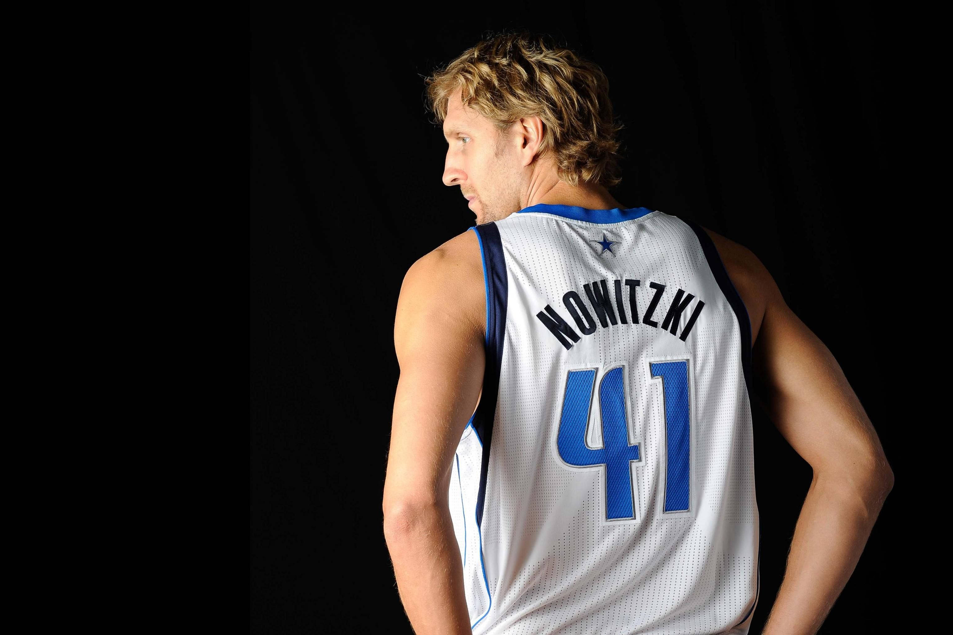 Dirk Nowitzki 桌布 壁紙 — 一名籃球運動員身穿白色和藍色球衣，背面印有「NOWITZKI 41」，側身站在黑色背景前。