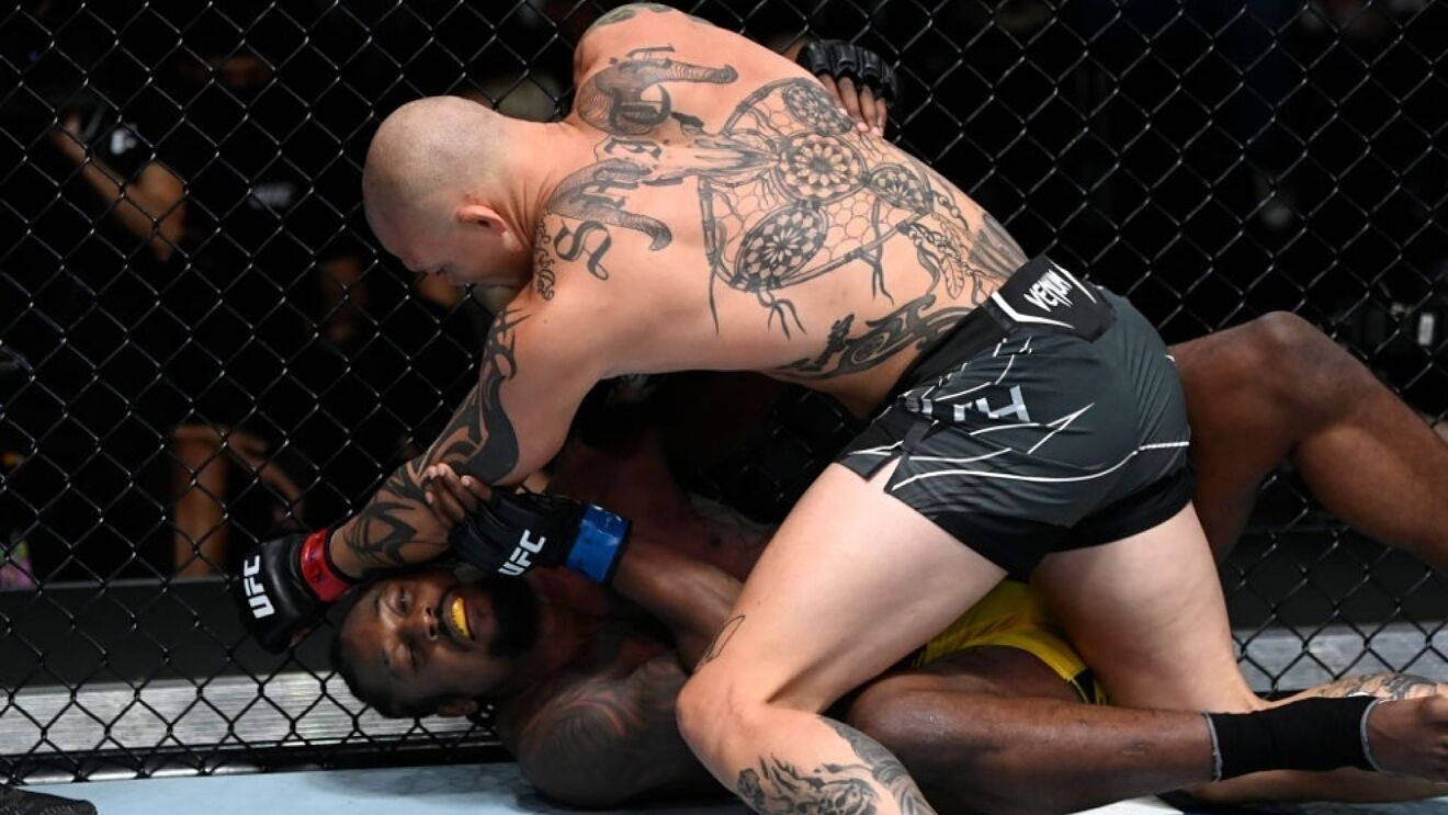 MMA 桌布 壁紙 — 一名紋身戰士穿著黑色短褲，在UFC八角籠內壓制對手在地面。