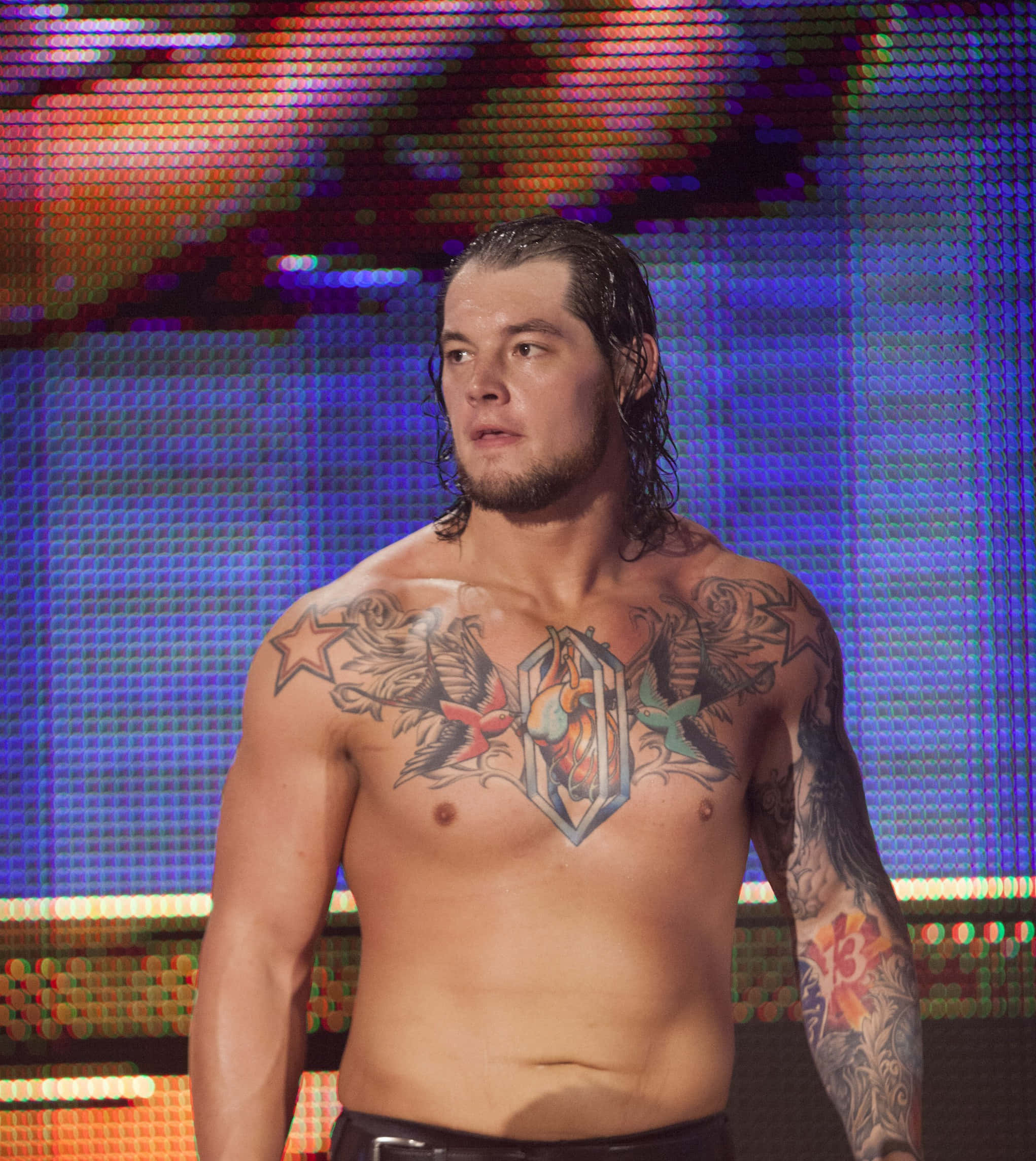 WWE 桌布 壁紙 — 一名紋身摔角手在充滿活力的舞台燈光下赤裸上身，身後是色彩繽紛的像素化螢幕。