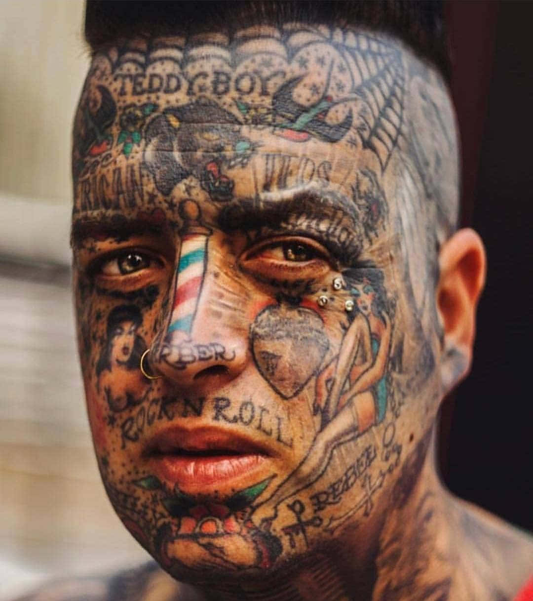 Face Tattoo 桌布 壁紙 — 一名紋身濃密的男子臉部特寫，複雜的圖案覆蓋其皮膚，並有多處面部穿孔。