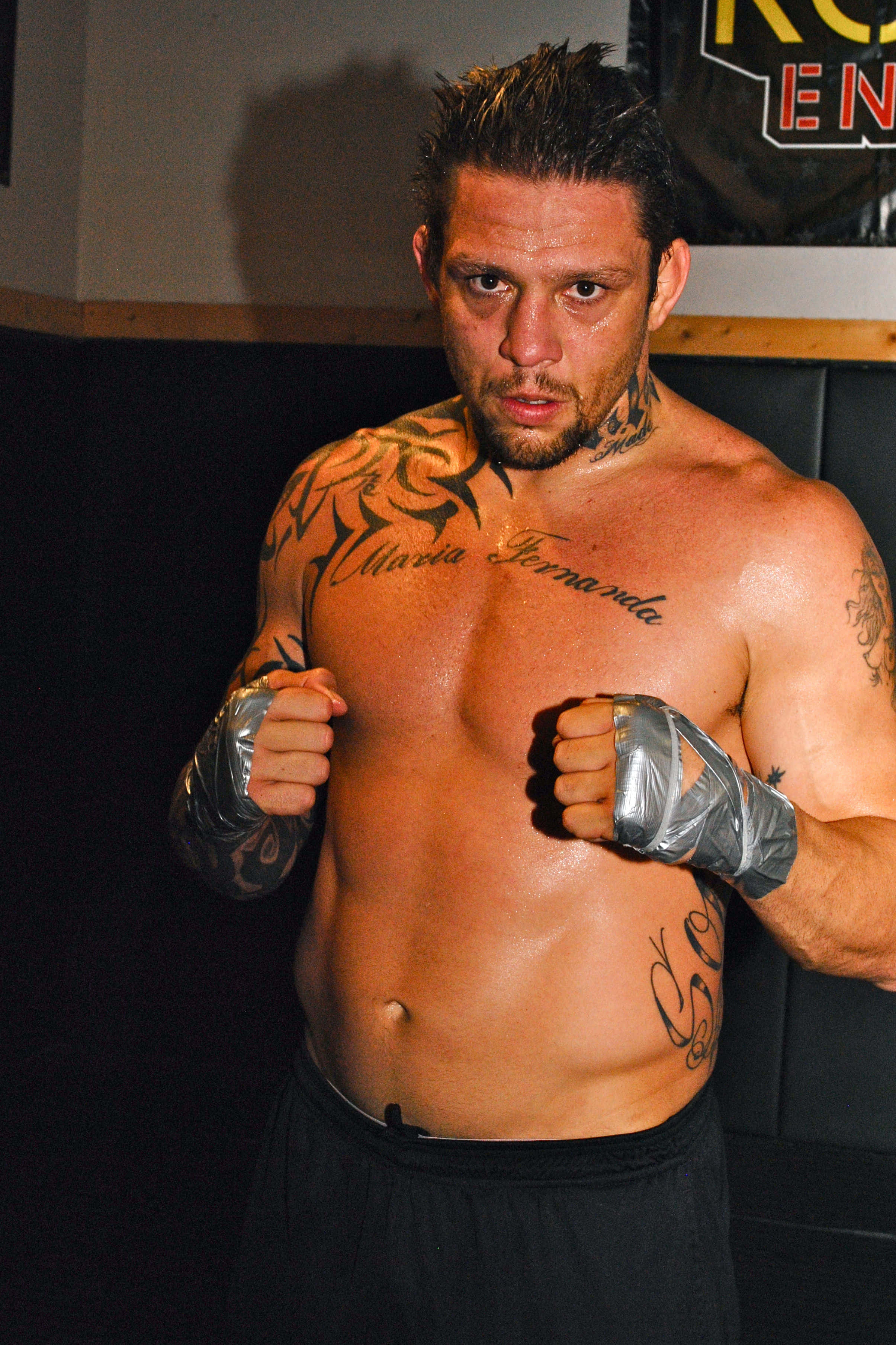 MMA 桌布 壁紙 — 一名紋身男拳手，拳頭纏著銀色繃帶，在昏暗的健身房中凝視著。