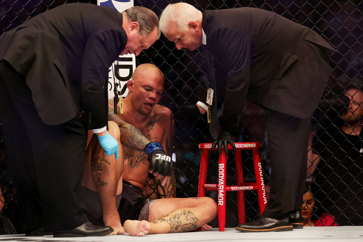 MMA 桌布 壁紙 — 一名紋身鬥士筋疲力竭地坐在UFC八角籠內，兩名官員在比賽後檢查他。